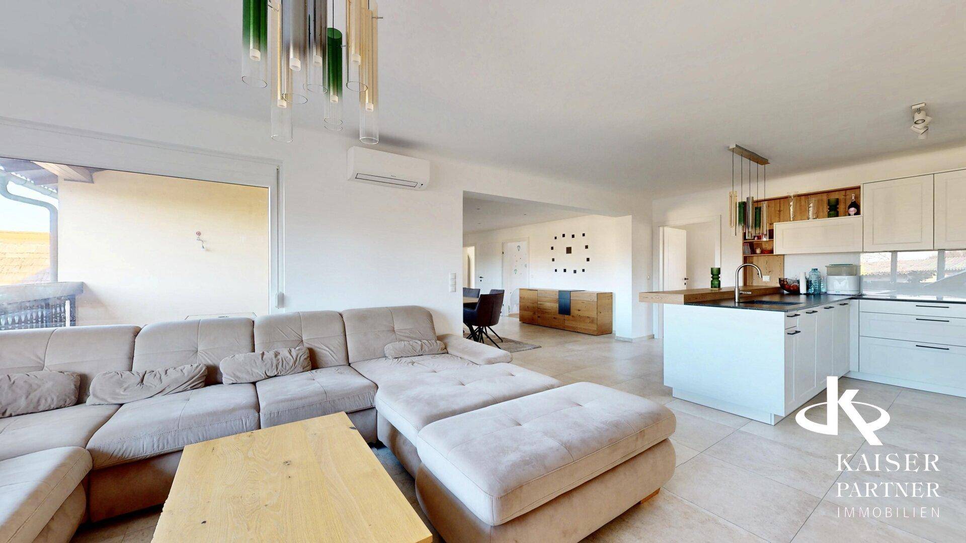Heller, offener Wohn-Essbereich mit moderner Küche, großem Sofa und Zugang zum Balkon.