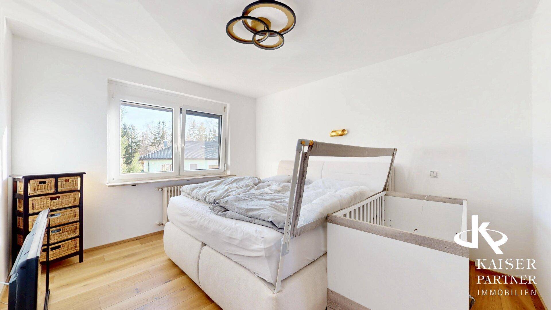 Helles Schlafzimmer mit Doppelbett, Holzboden und Fenster mit Blick ins Grüne.