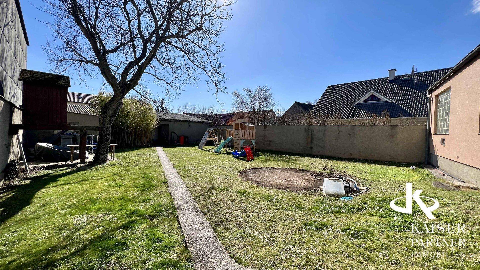 Weitläufiger Gartenbereich mit Rasen, altem Baum und Kinderspielgeräten.