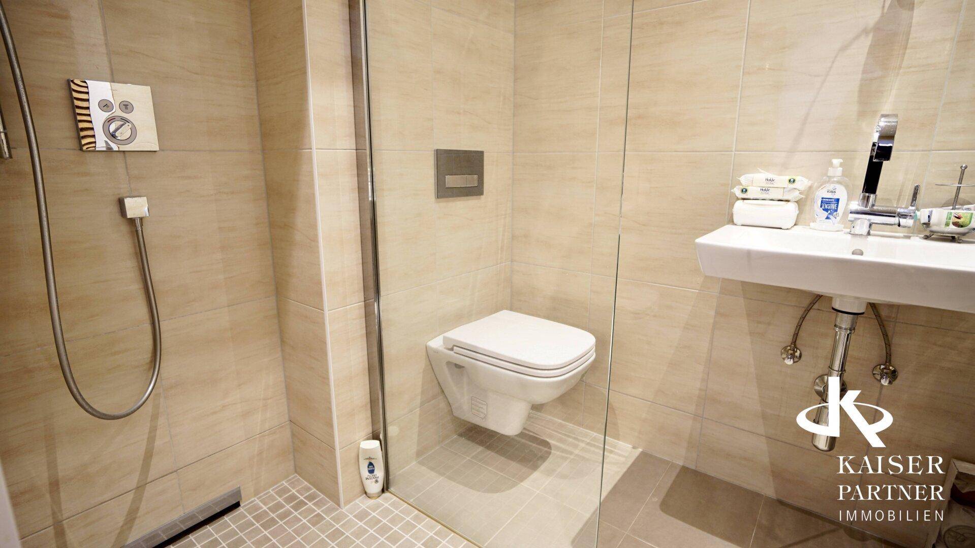 Modernes Badezimmer mit beigefarbenen Fliesen, ebenerdiger Dusche, wandhängendem WC und Einzelwaschbecken.