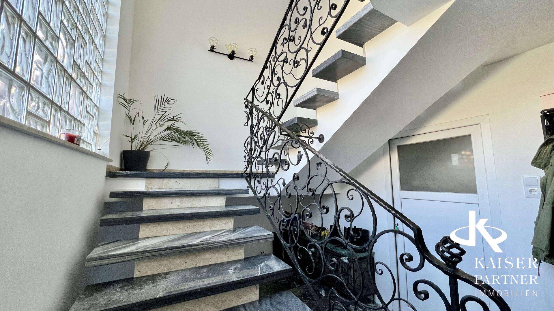 Elegante Treppe mit schmiedeeisernem Geländer und Marmorstufen, beleuchtet durch ein Glasbausteinfenster.