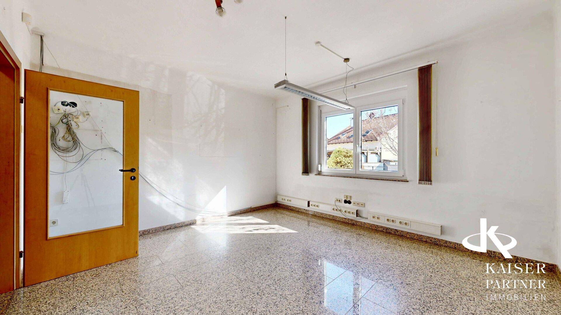Heller, leerer Raum mit Terrazzoboden und großen Fenstern.