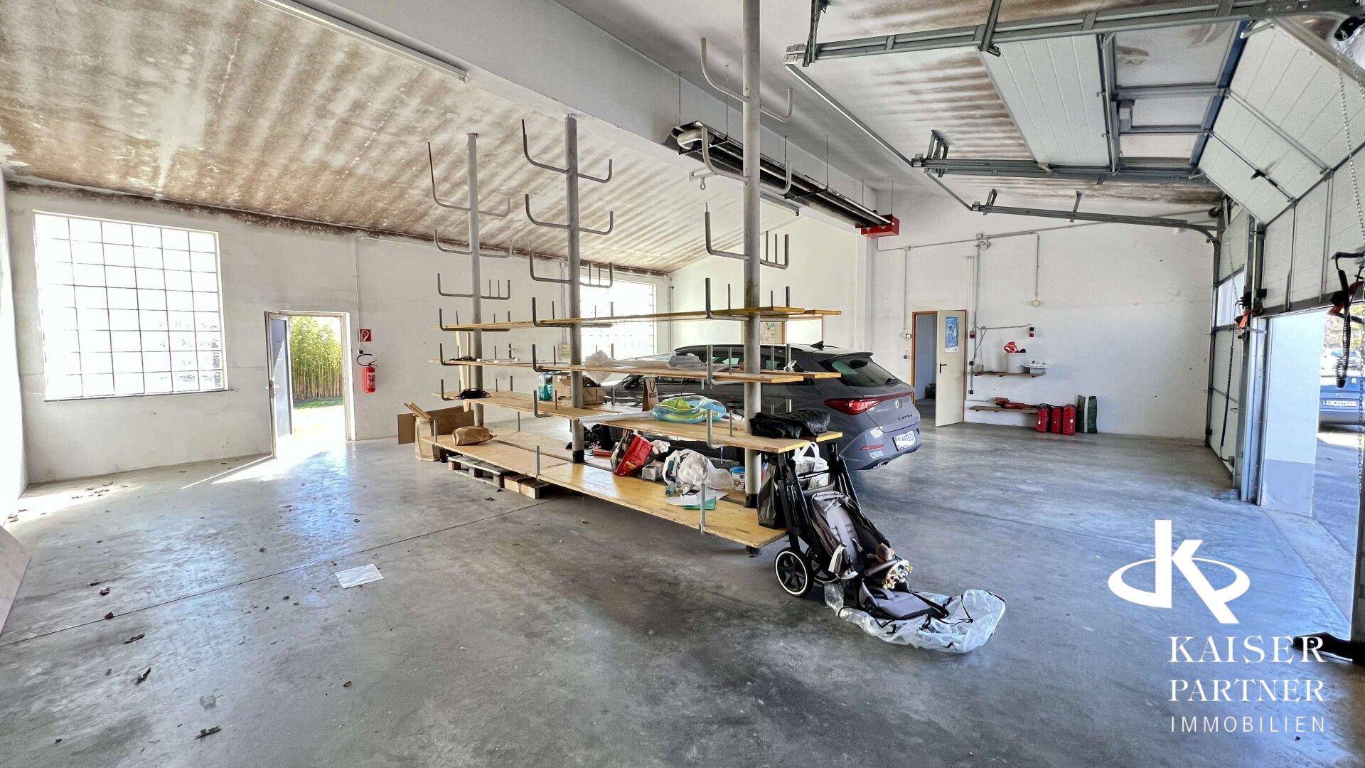 Geräumige Garage mit Betonboden, Lagerregalen und Platz für Fahrzeuge, ideal als Werkstatt.