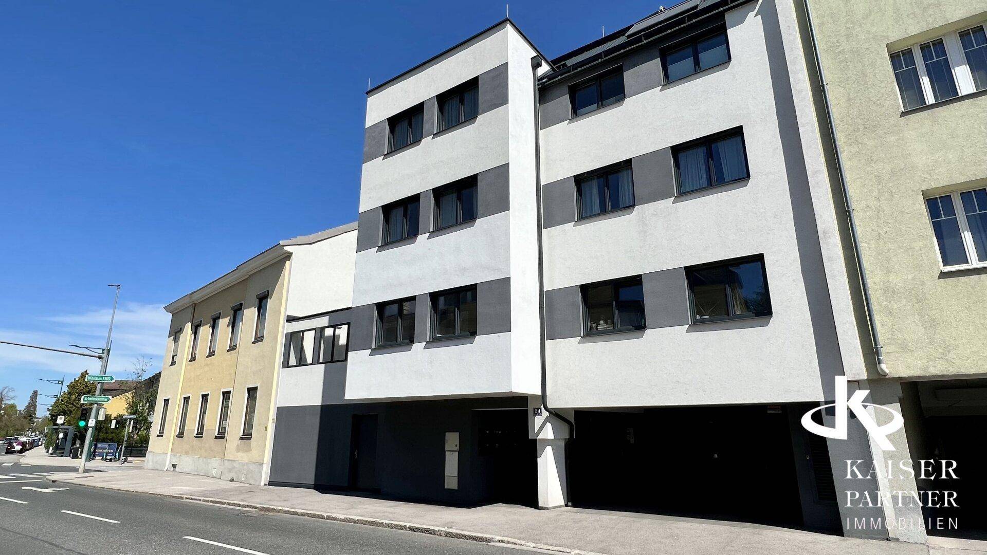 Moderne Fassade eines Mehrfamilienhauses mit klaren Linien und großen Fenstern an einer Straße.