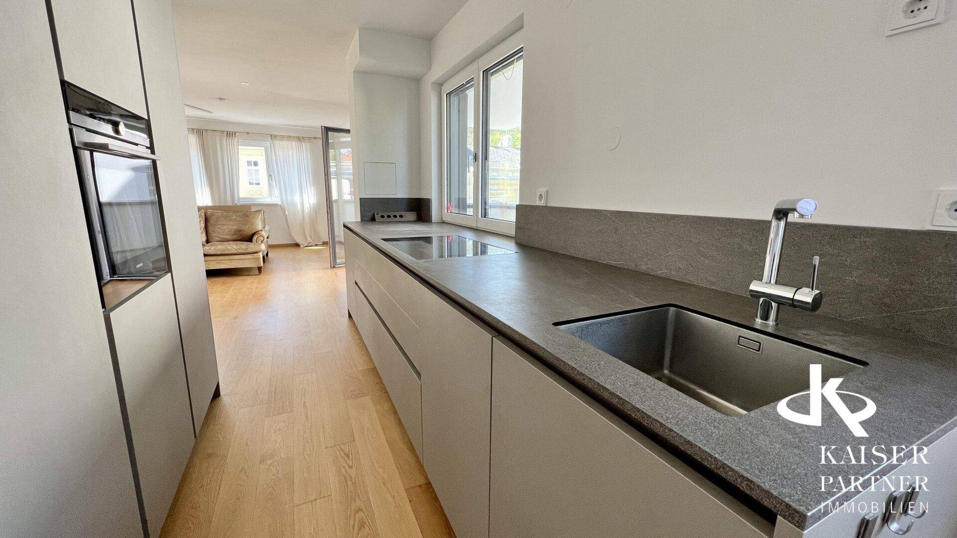Moderne Küche mit grauen Arbeitsplatten und integrierten Geräten, offen zum Wohnbereich.