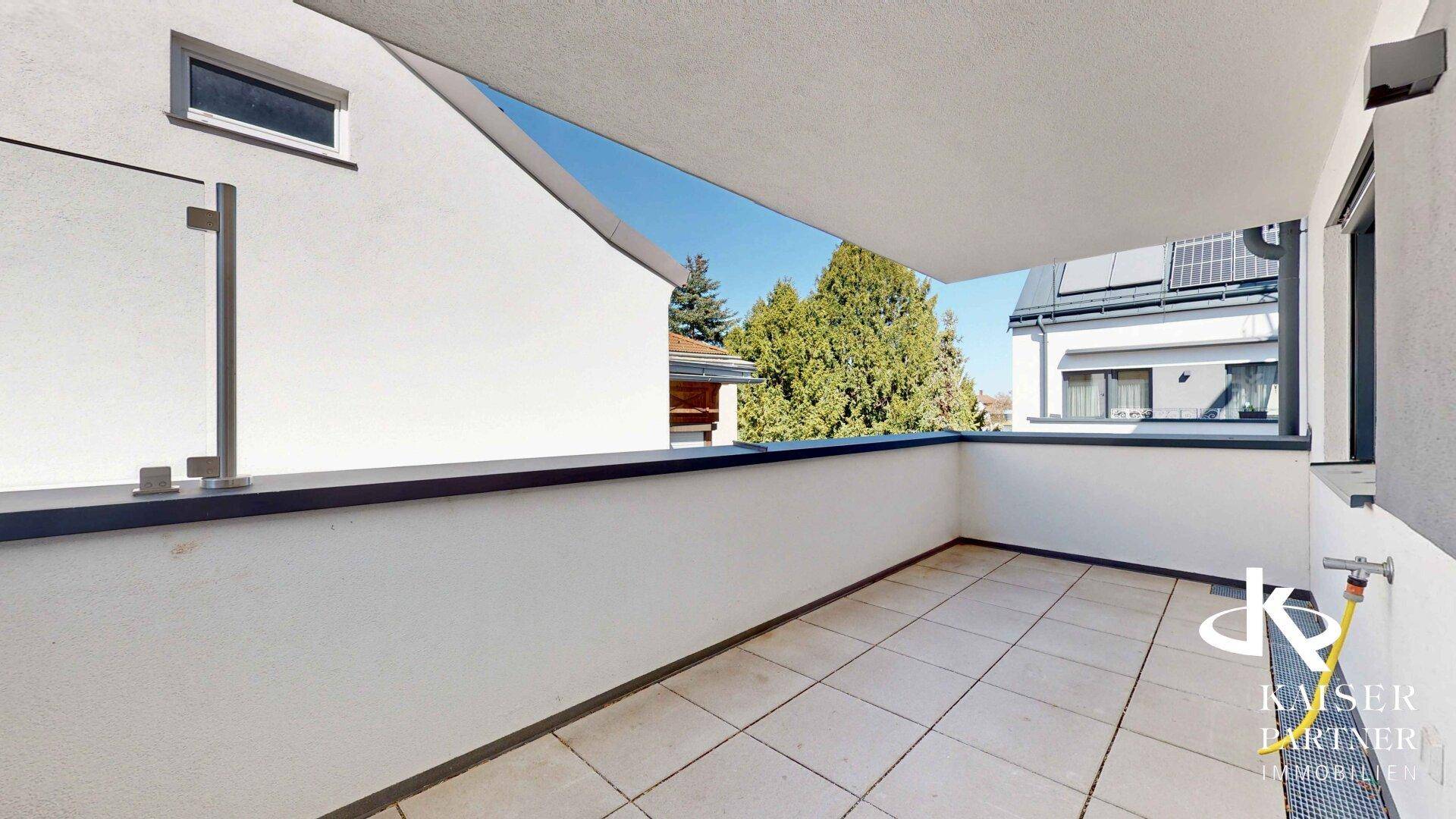 Sonniger Balkon mit Fliesenboden und seitlichem Blick auf grüne Bäume und die Umgebung.