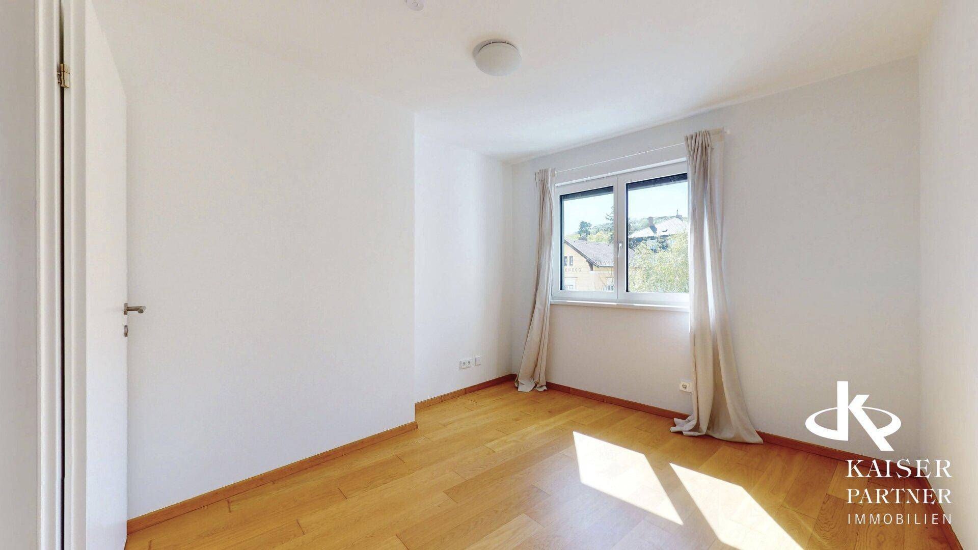 Helles Schlafzimmer mit Holzparkettboden und großem Fenster, das viel Tageslicht hereinlässt.