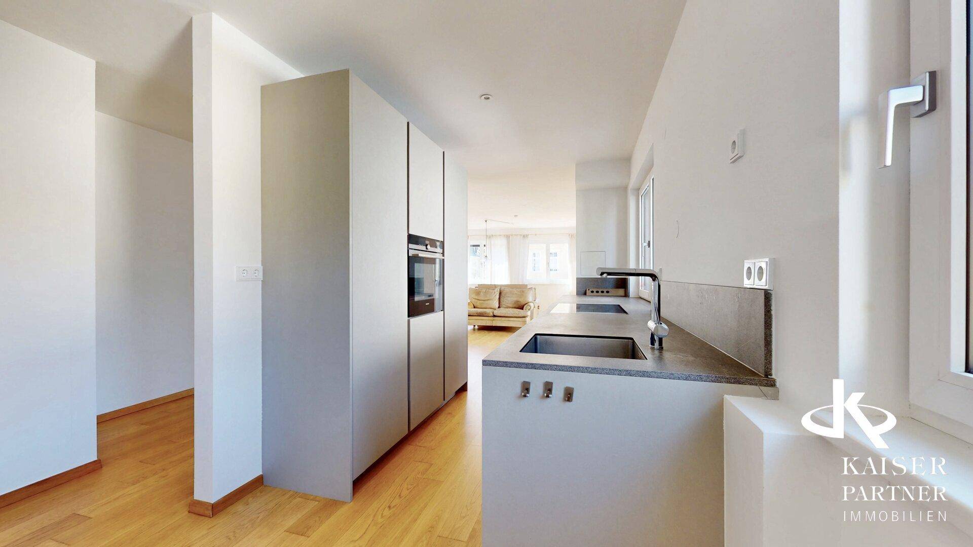 Stilvolle Küche mit minimalistischen Schränken und grauer Arbeitsplatte, nahtlos in den Wohnraum integriert.