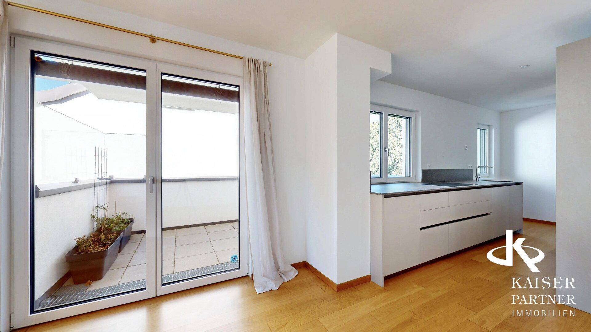Heller Wohnbereich mit Balkonzugang und Blick auf die moderne, offene Küchenzeile.