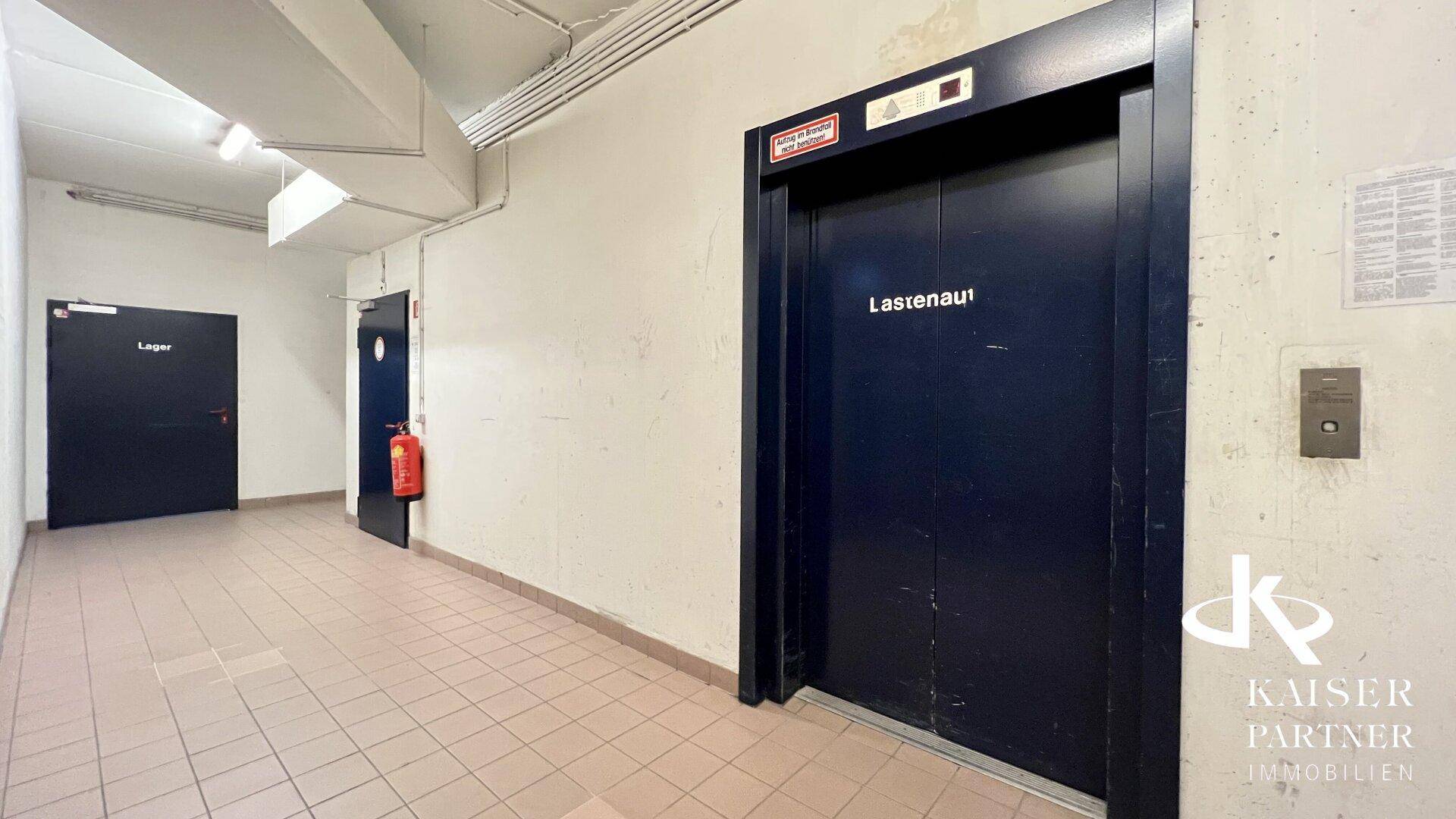 Flur im Untergeschoss mit Fliesenboden, zwei Türen und einem Lastenaufzug.