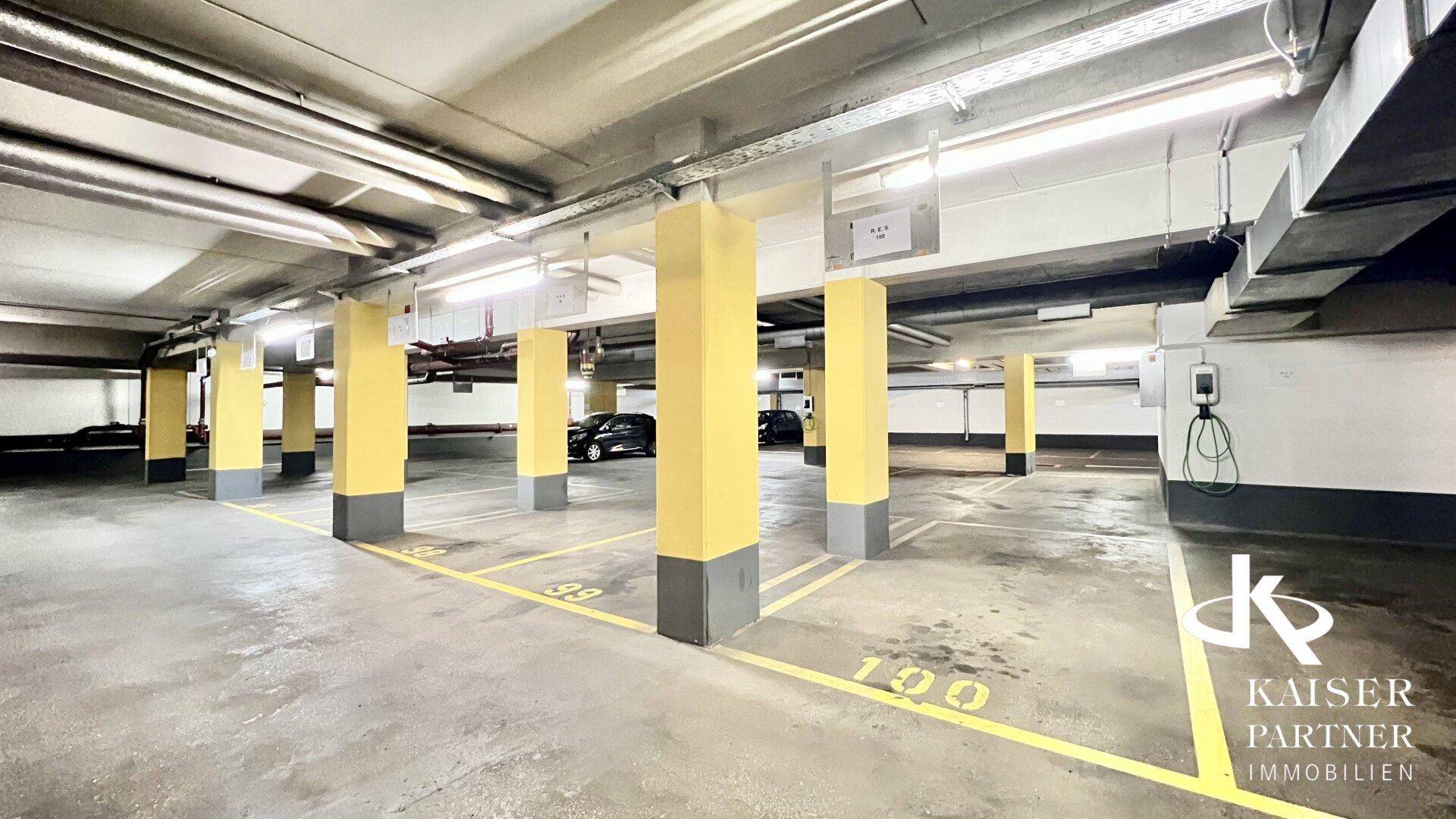 Geräumige Tiefgarage mit markierten Stellplätzen, gelben Säulen und Deckenbeleuchtung.