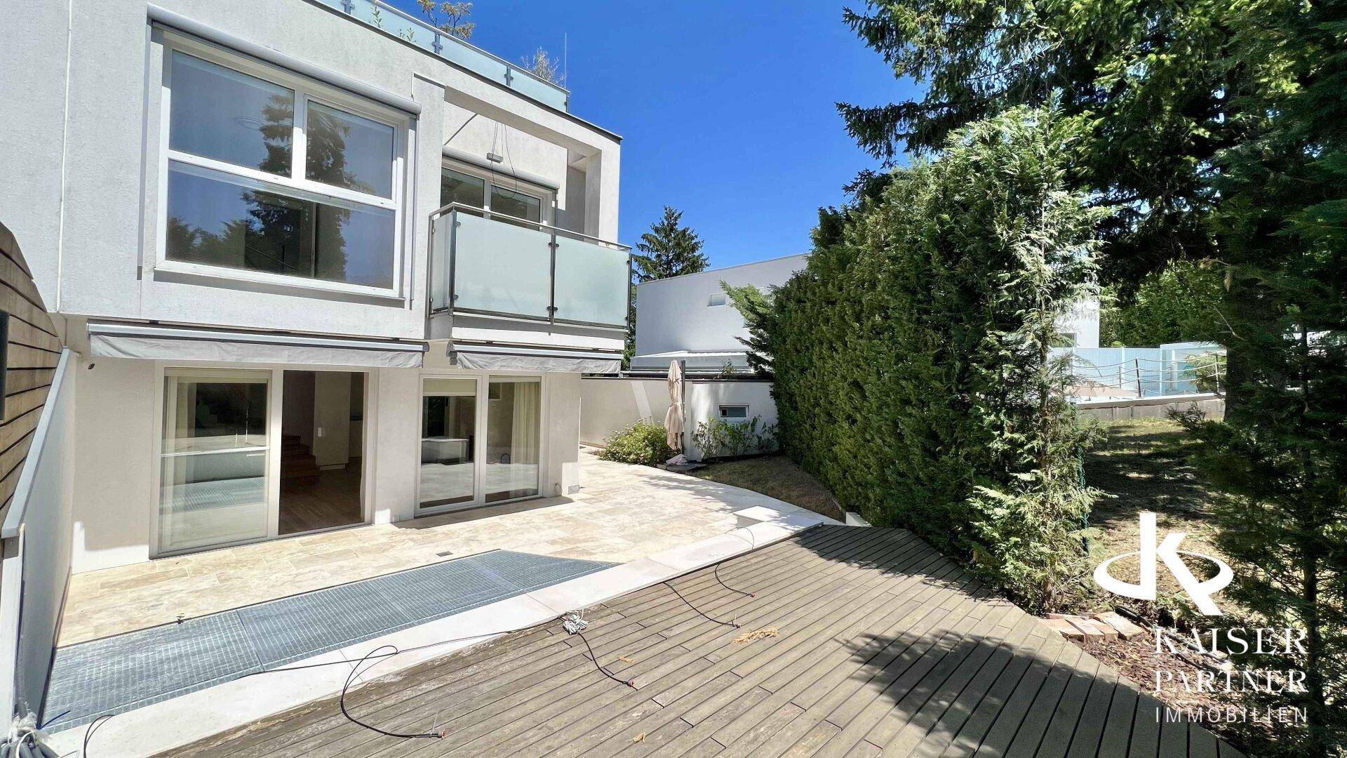 Moderne Gebäudefassade mit großzügiger Terrasse, großen Glasfronten und umgebender Hecke.