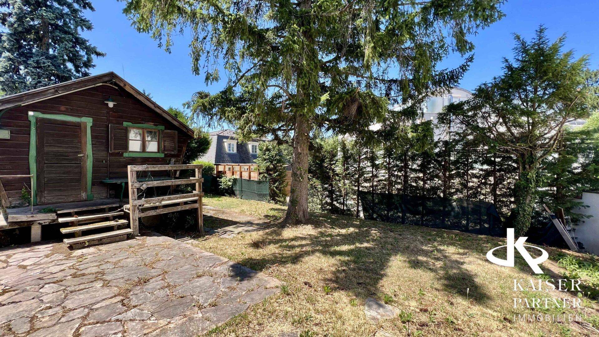 Naturbelassener Gartenbereich mit altem Baumbestand, Rasenfläche und einem rustikalen Gartenhaus.