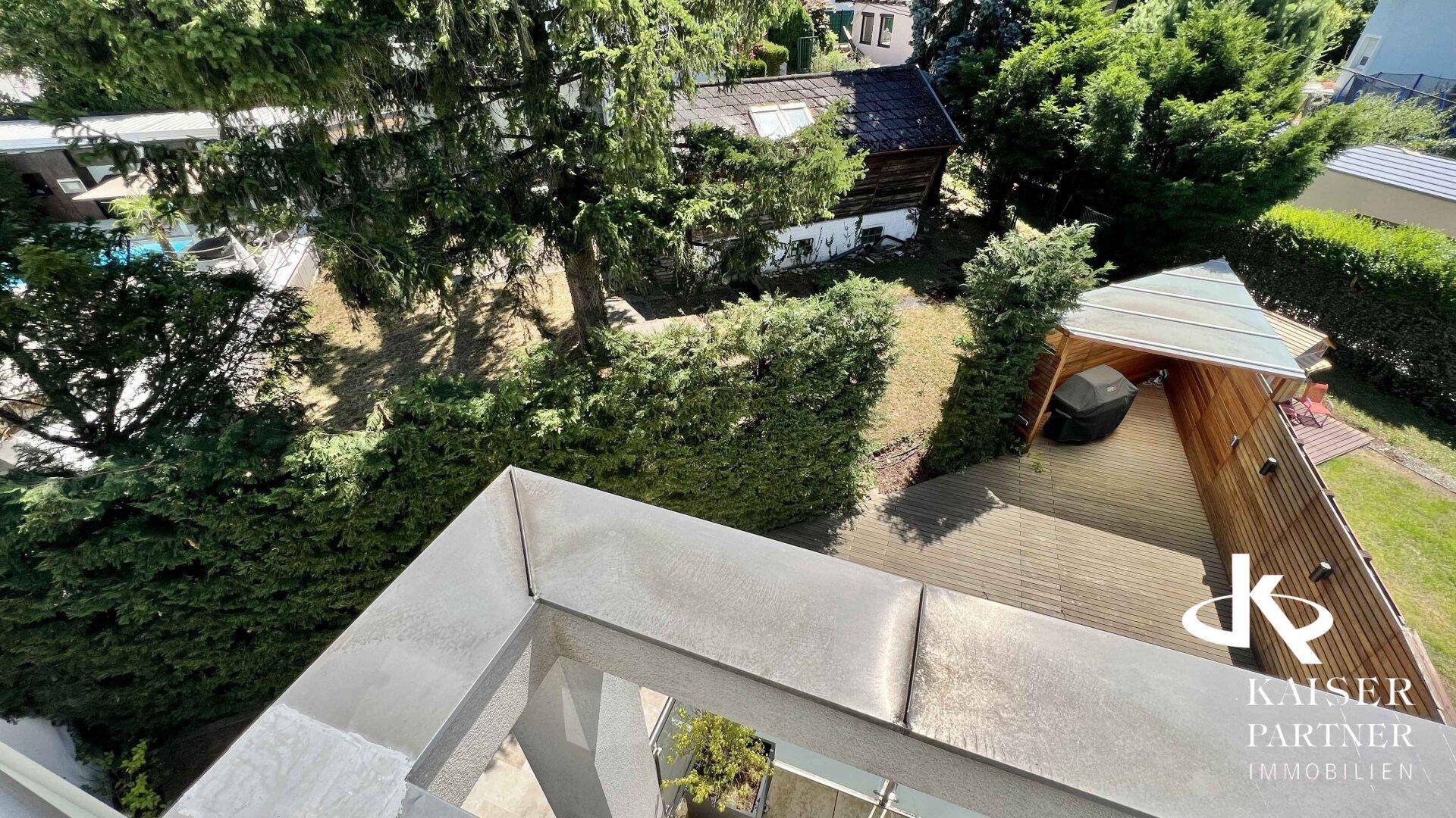 Vogelperspektive des Außenbereichs mit Holzterrasse, Grillplatz und üppiger grüner Umgebung.