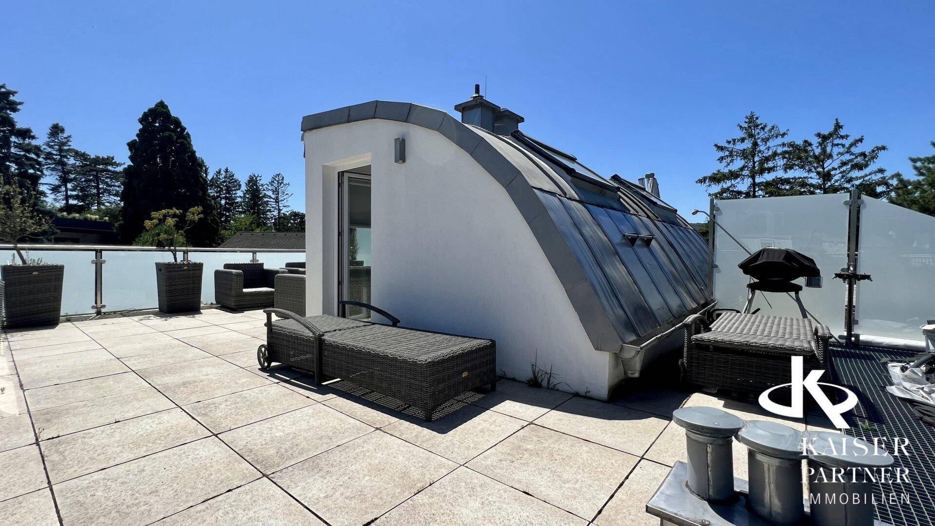 Großzügige Dachterrasse mit Fliesenboden, Liegestuhl und Blick auf die umliegende grüne Landschaft.