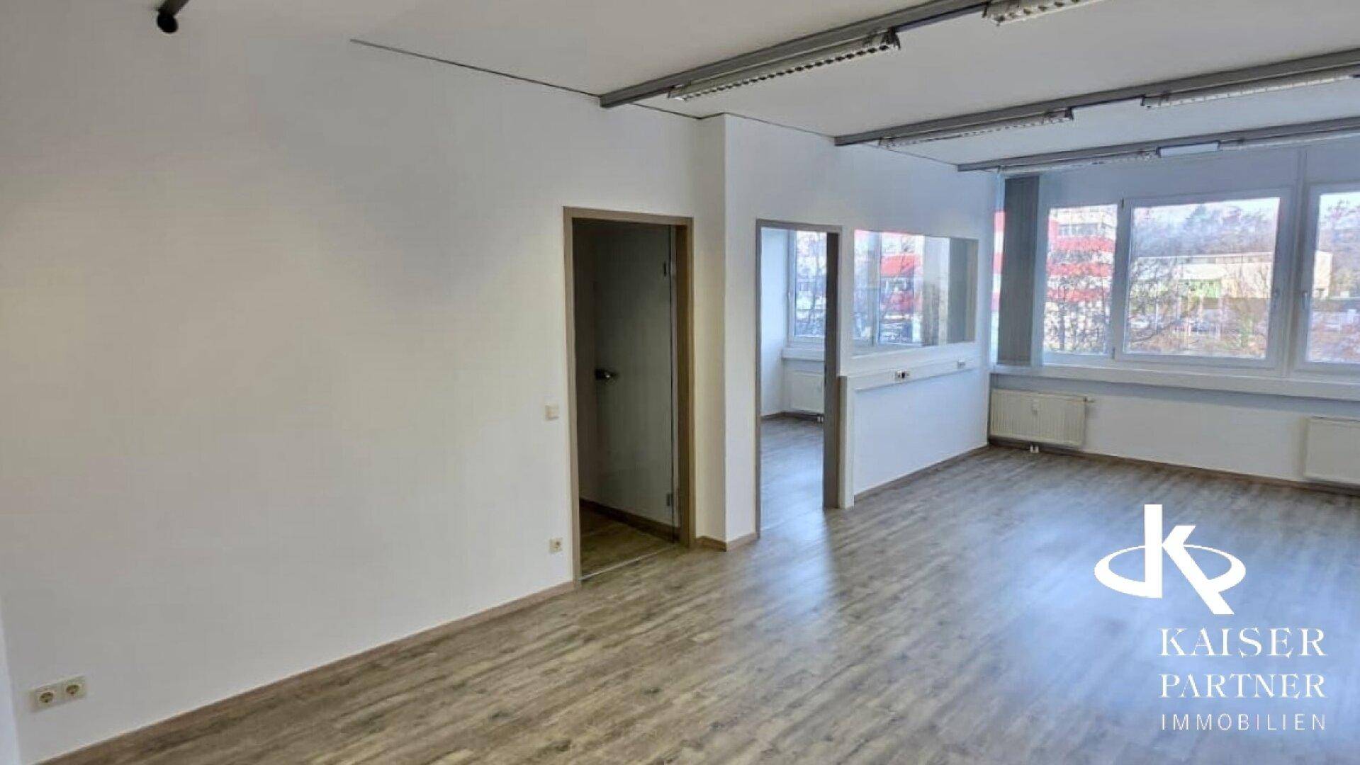Helles Büro mit Laminatboden, weißen Wänden und einer Tür, die zu einem weiteren Raum führt.
