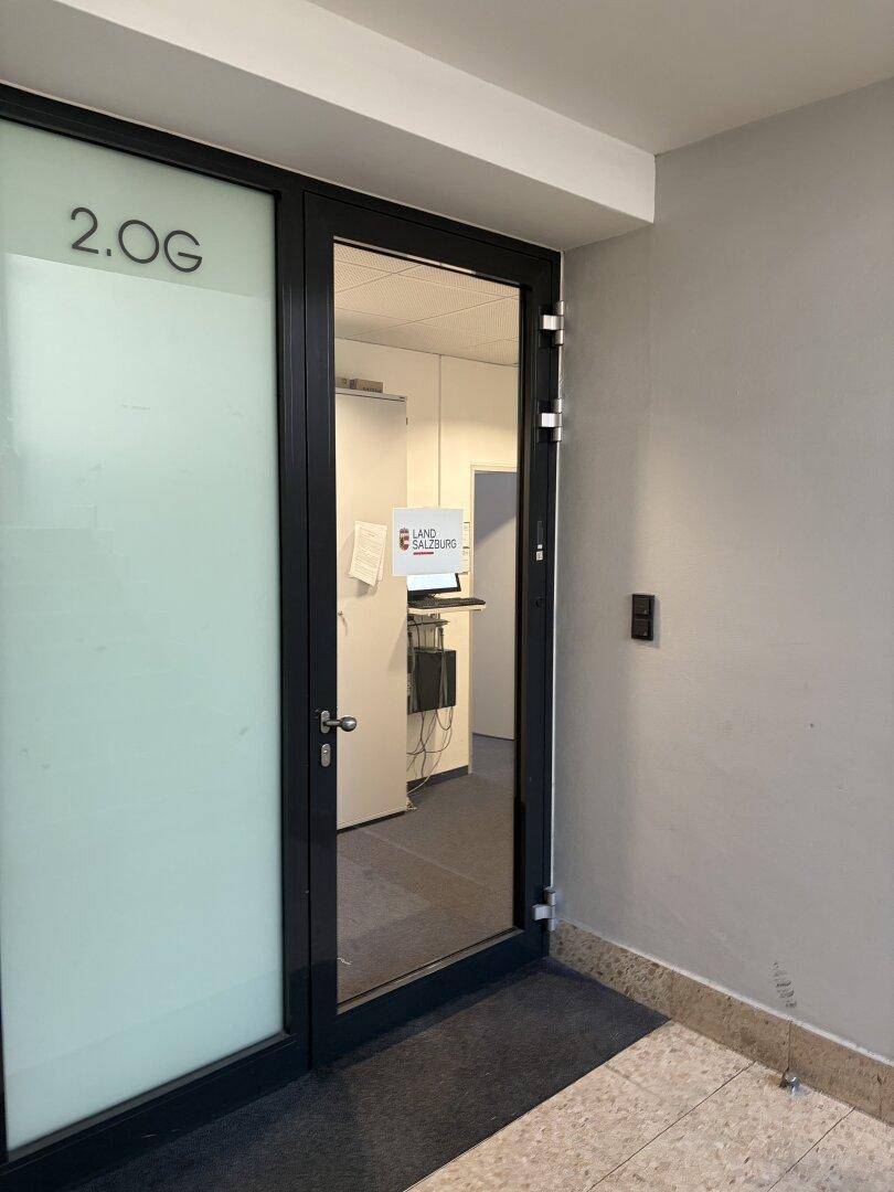 Eingangstür zu einem Büro im zweiten Obergeschoss, mit Glaspaneelen und einem Hinweisschild.