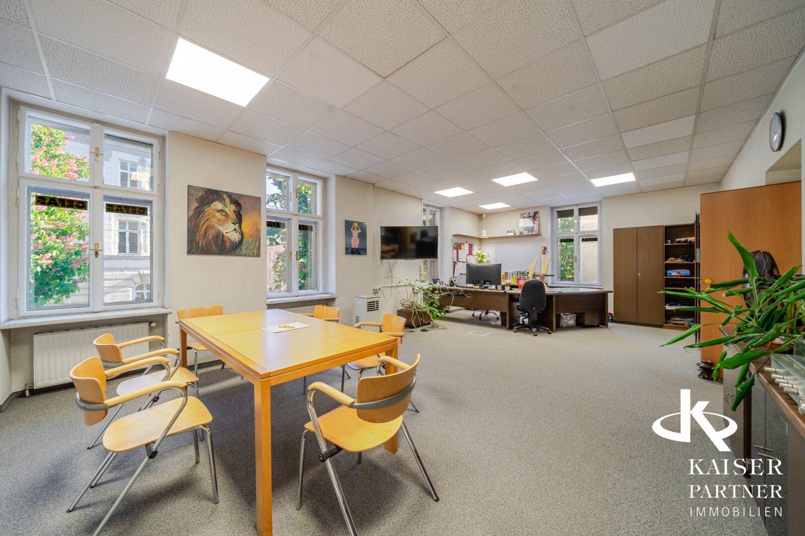 Flexibler Bürobereich mit Besprechungstisch und weiteren Arbeitsplätzen im Hintergrund.