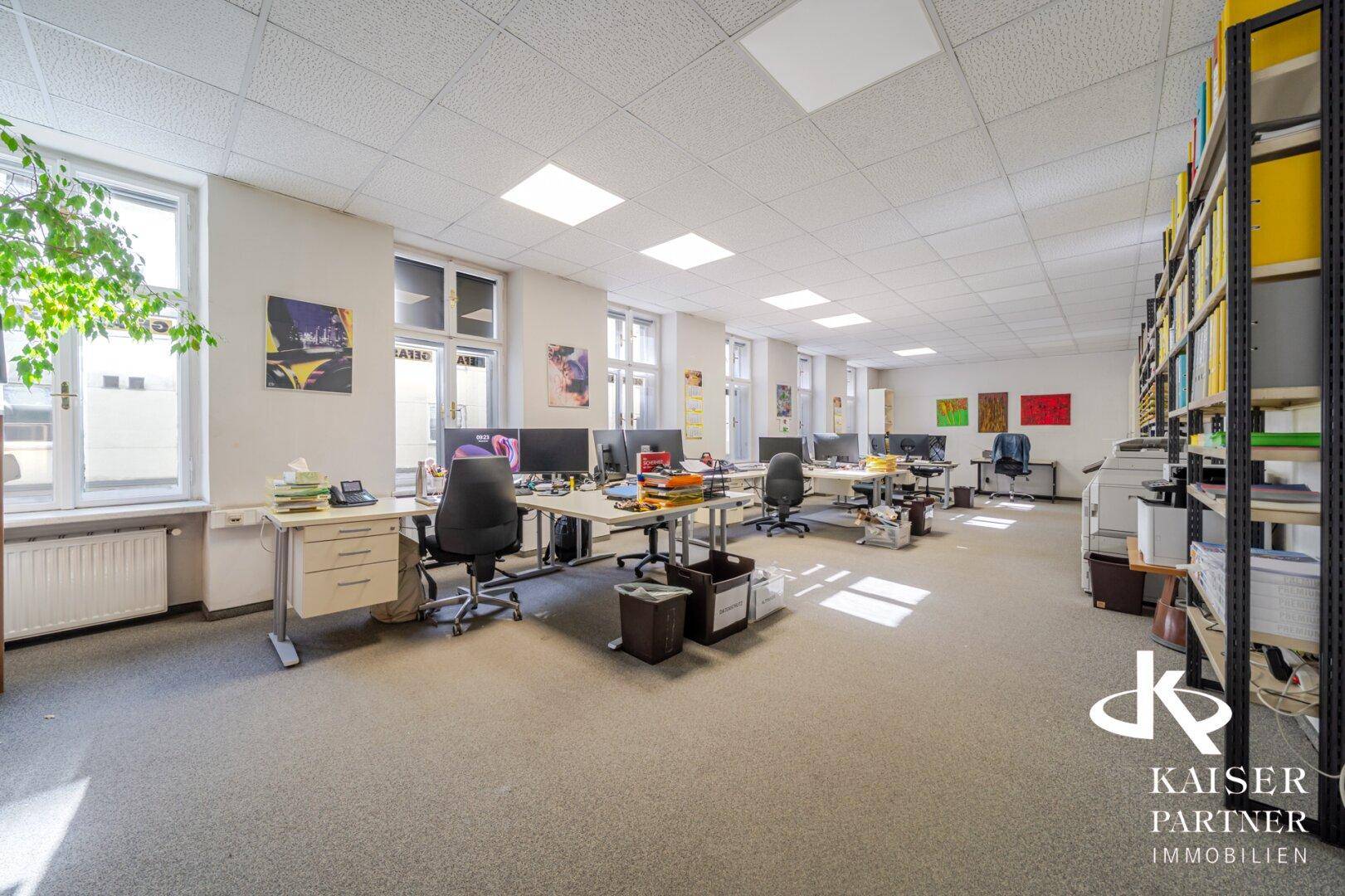 Geräumiges Büro mit vielen Arbeitsplätzen, viel Tageslicht und Regalen.