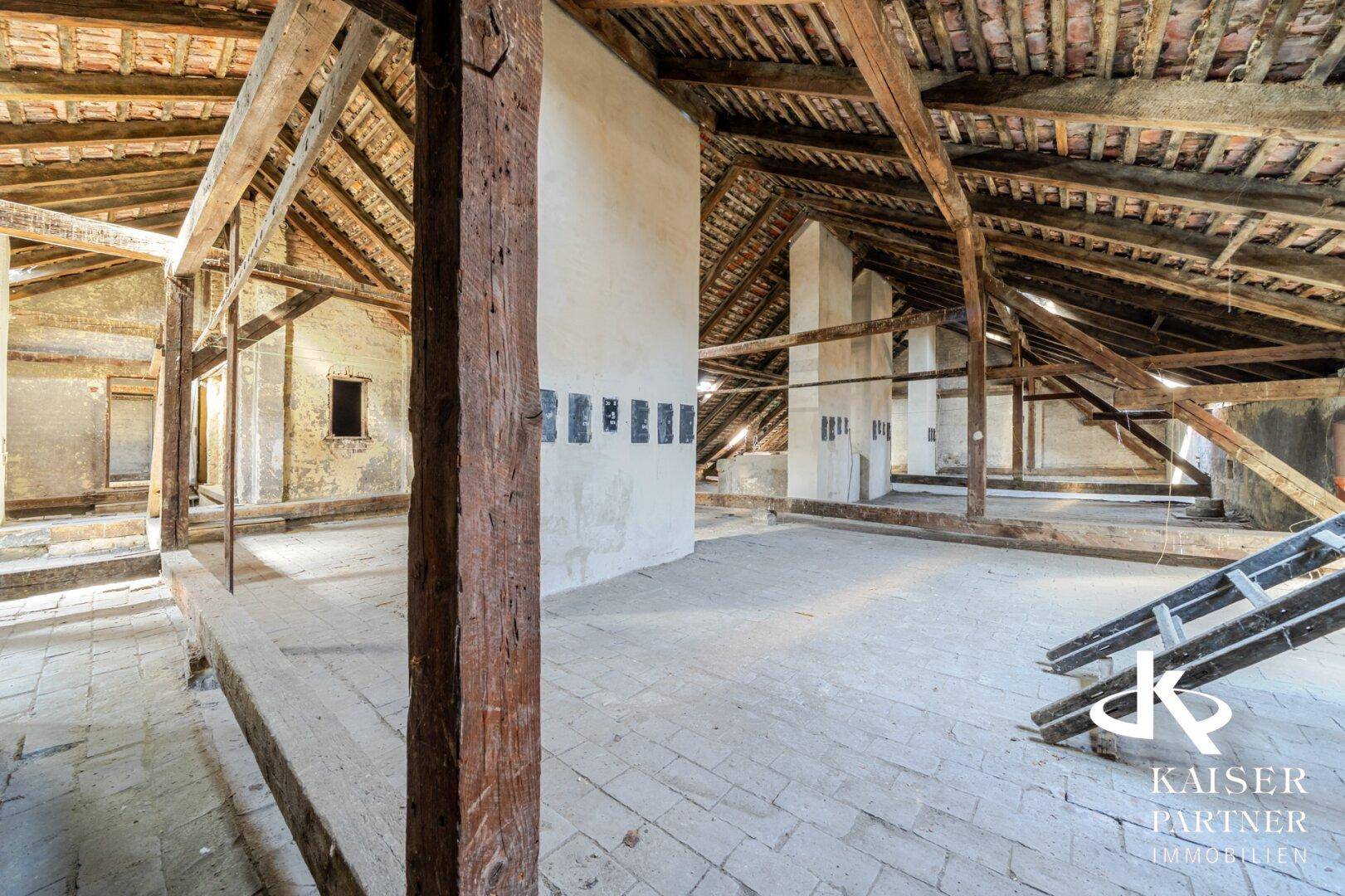 Großer, unfertiger Dachbodenbereich mit robusten Holzbalken und Ziegeln, ideal für zukünftige Entwicklung.