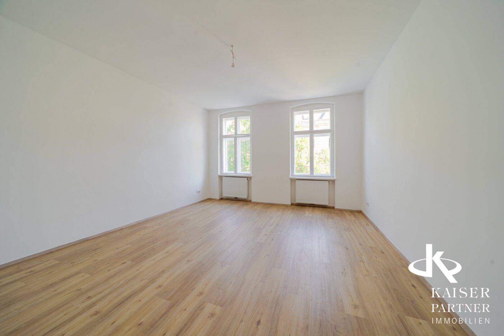 Leerer Raum mit hellem Laminatboden und zwei großen Fenstern, bereit zur Einrichtung.