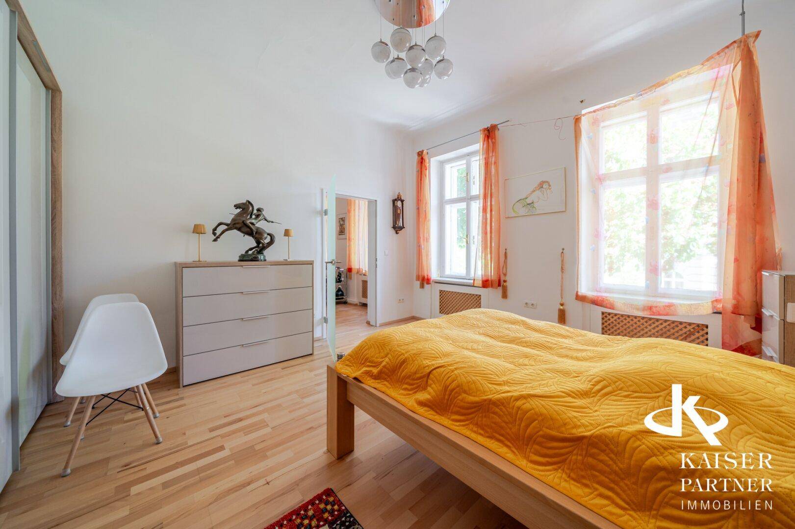 Gemütliches Schlafzimmer mit Holzboden, hellem Bett und großen Fenstern.