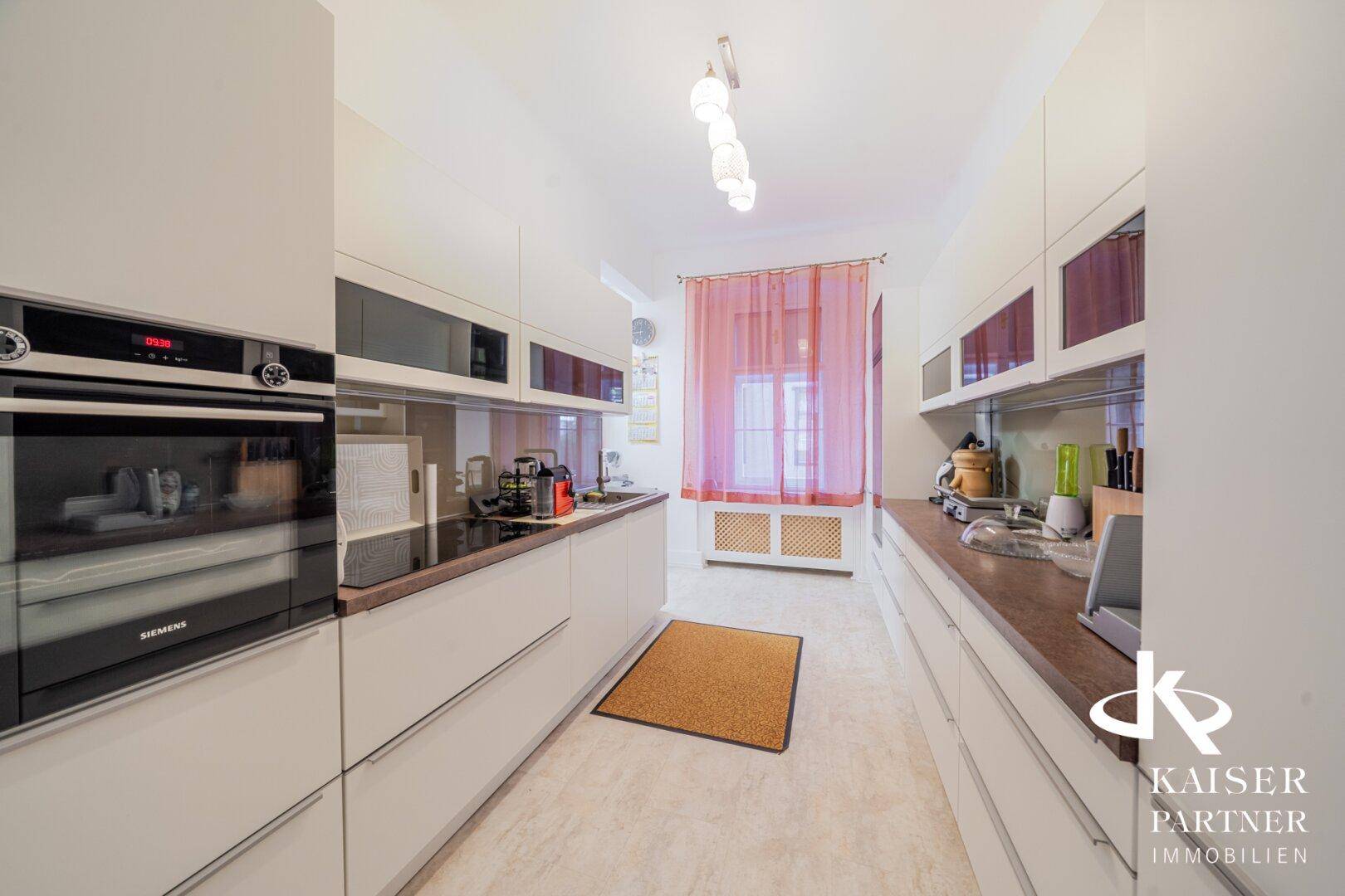 Moderne Küche mit weißen Schränken, integrierten Geräten und Fenster.