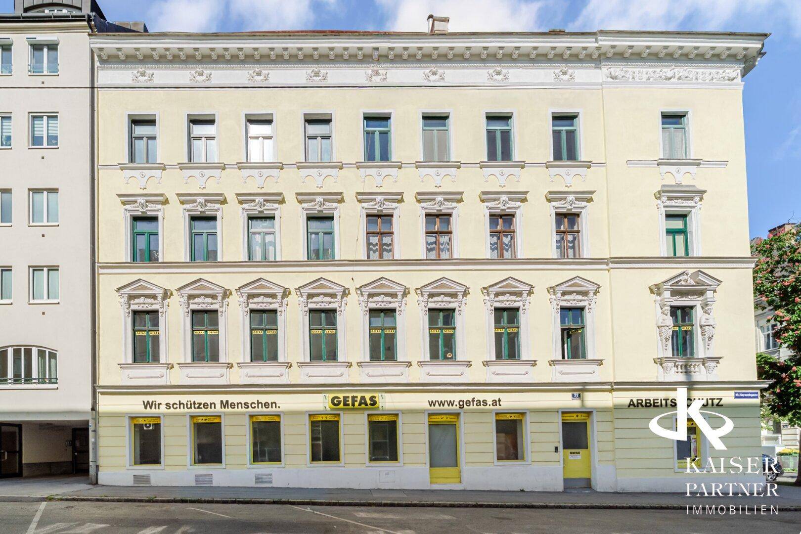 Klassische Fassade eines Altbaus mit vielen Fenstern und Geschäften im Erdgeschoss.