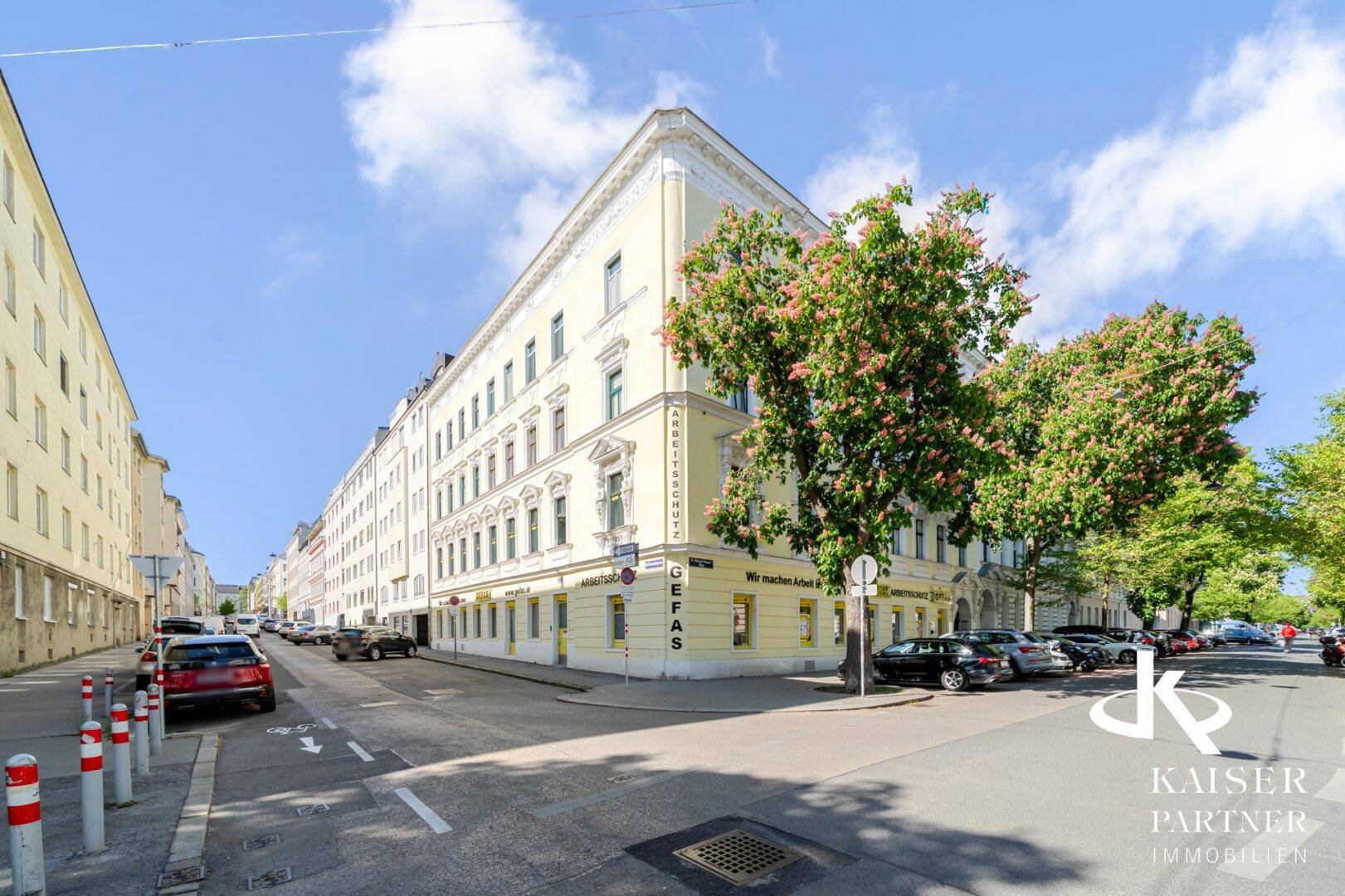 Eckgebäude mit historischer Architektur an einer städtischen Straße unter blauem Himmel.