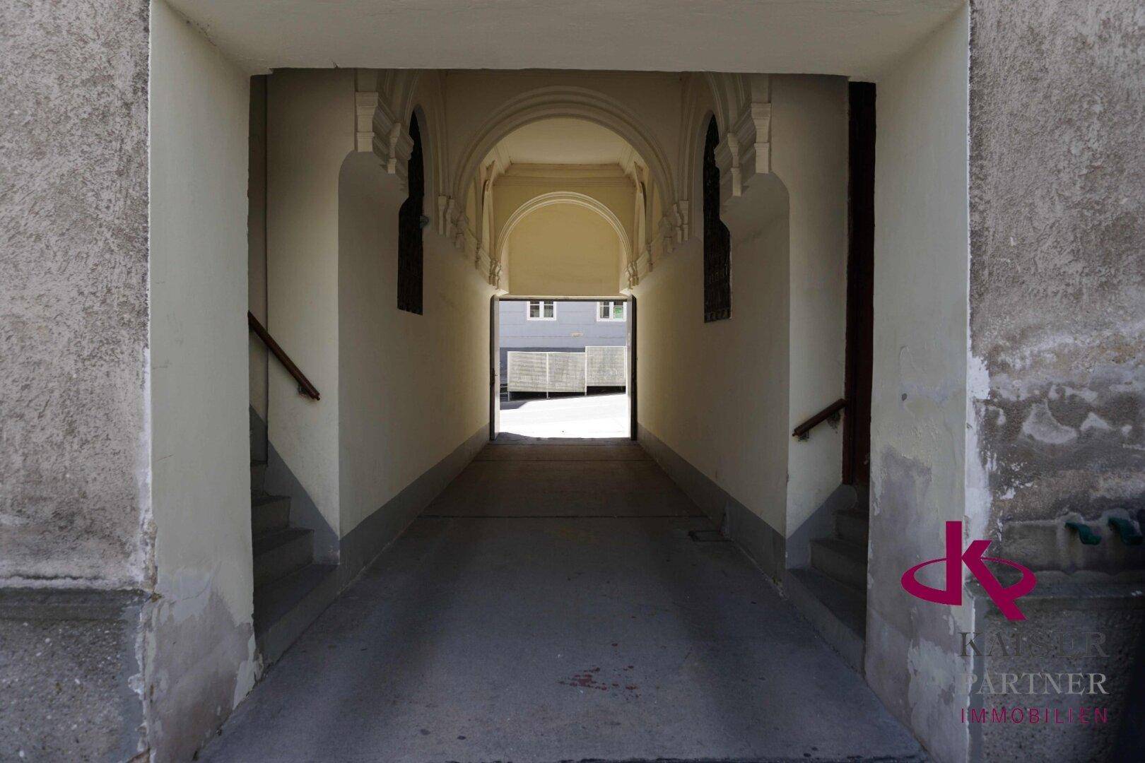 Historischer Durchgang mit verzierten Bögen und Stuckelementen, der zu einem Innenhof führt.