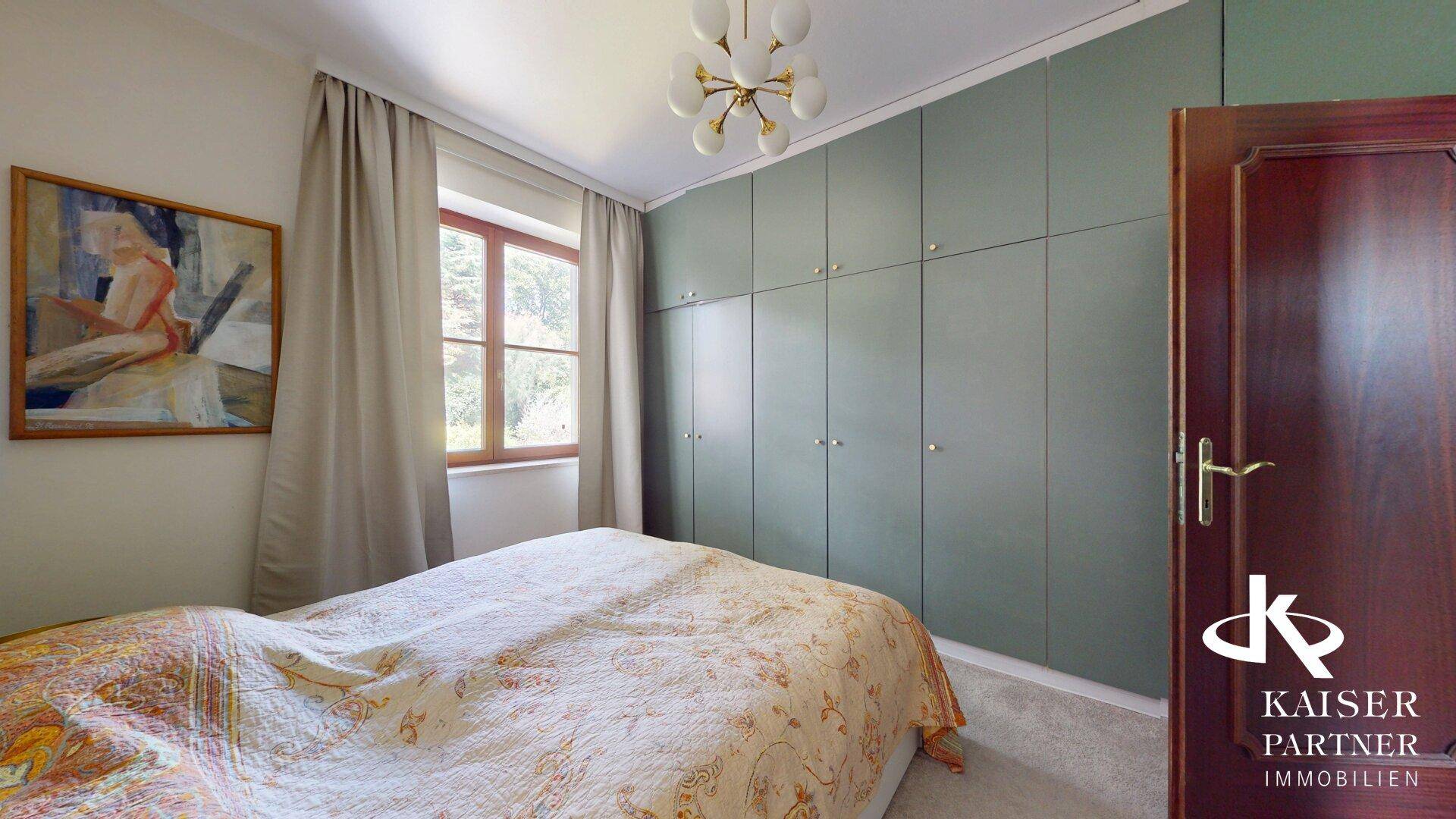 Schlafzimmer mit Einbauschränken, Doppelbett und Fenster mit Blick ins Grüne.