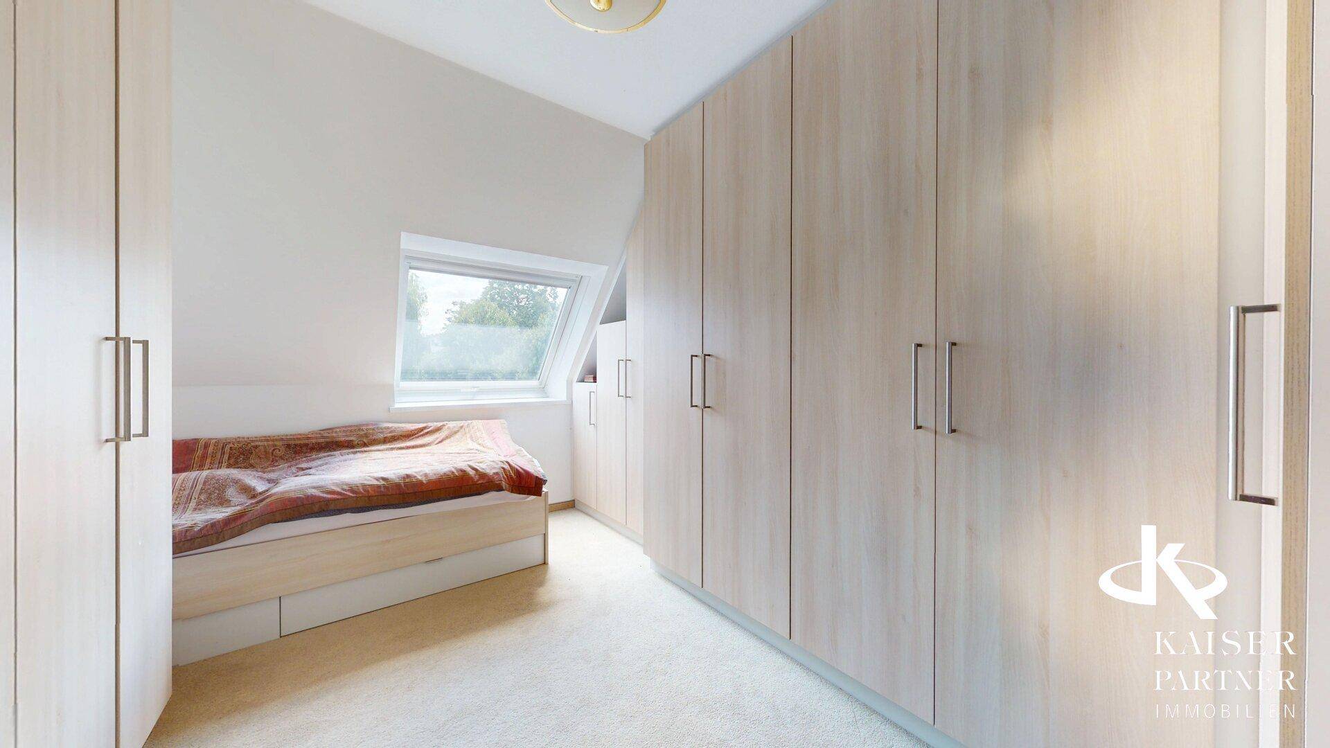 Schlafzimmer im Dachgeschoss mit Einbauschränken, Bett und Dachfenster.