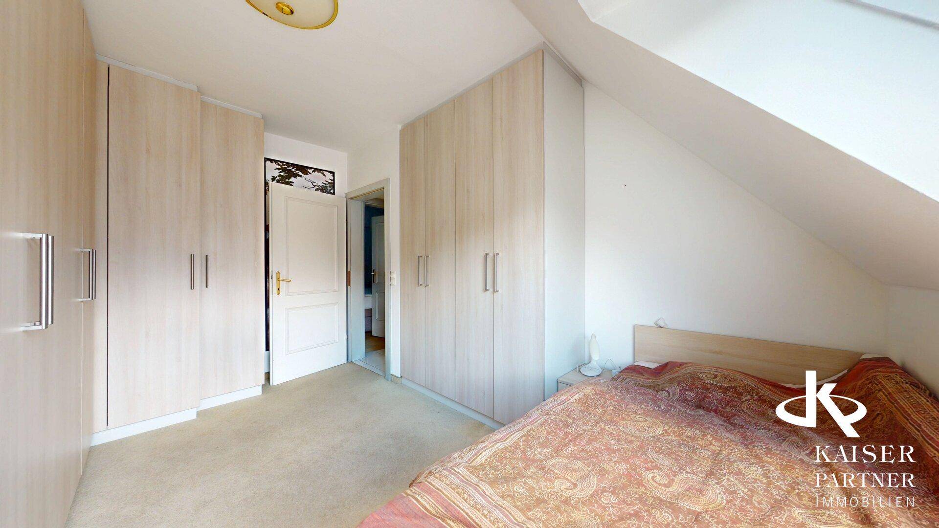 Schlafzimmer im Dachgeschoss mit Einbauschränken, Bett und hellem Teppichboden.