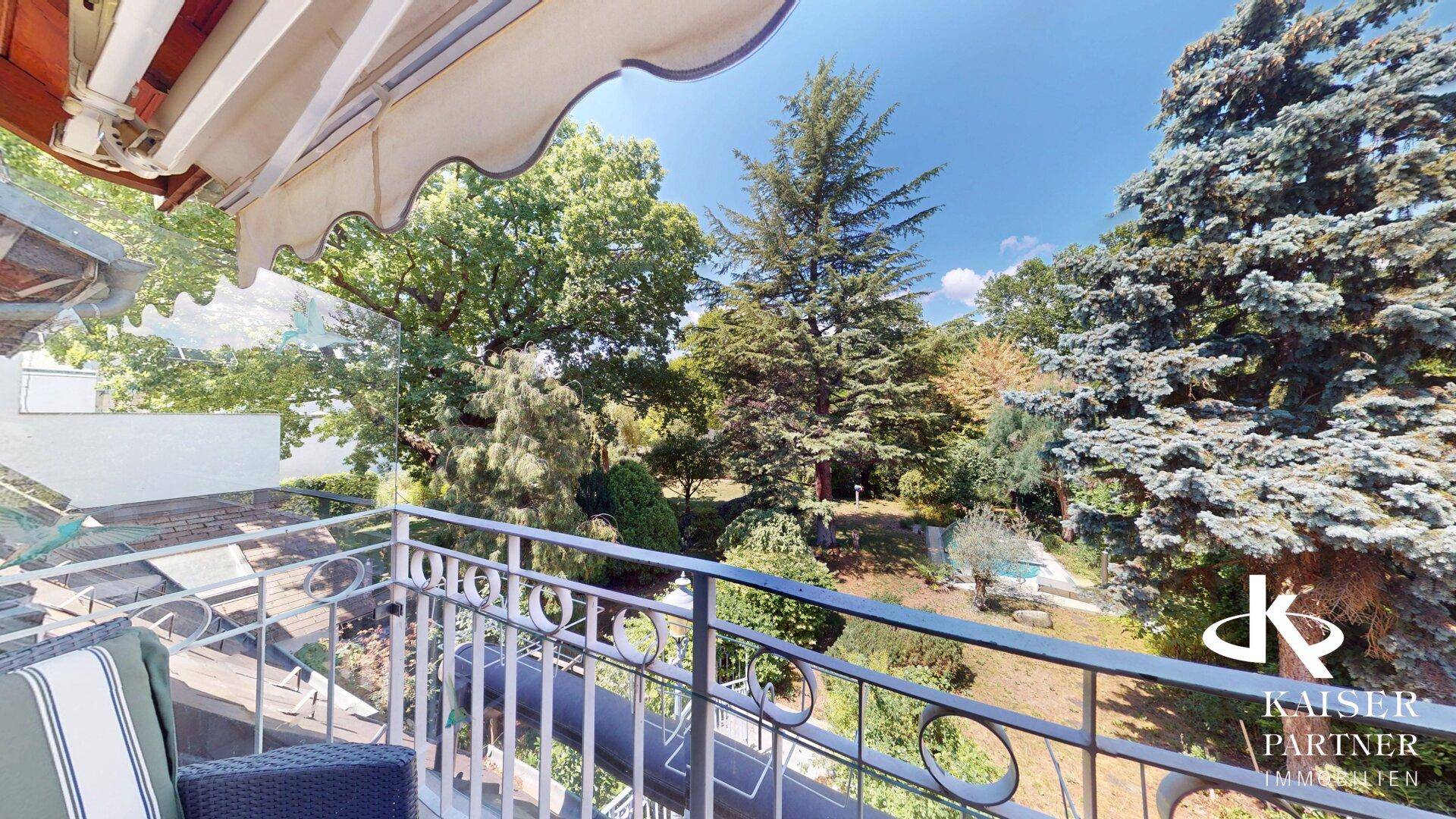 Balkon mit schmiedeeisernem Geländer und weitem Blick über den grünen Garten.