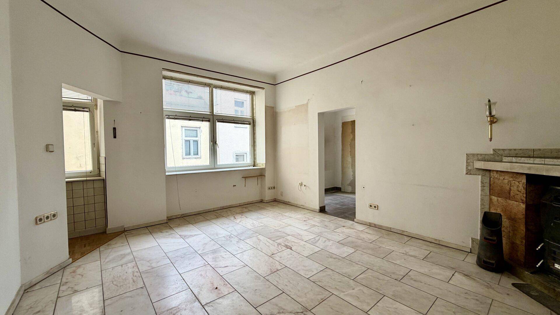 Helles Wohnzimmer mit Fliesenboden, Fenster und Kamin, bietet Potenzial für moderne Gestaltung.