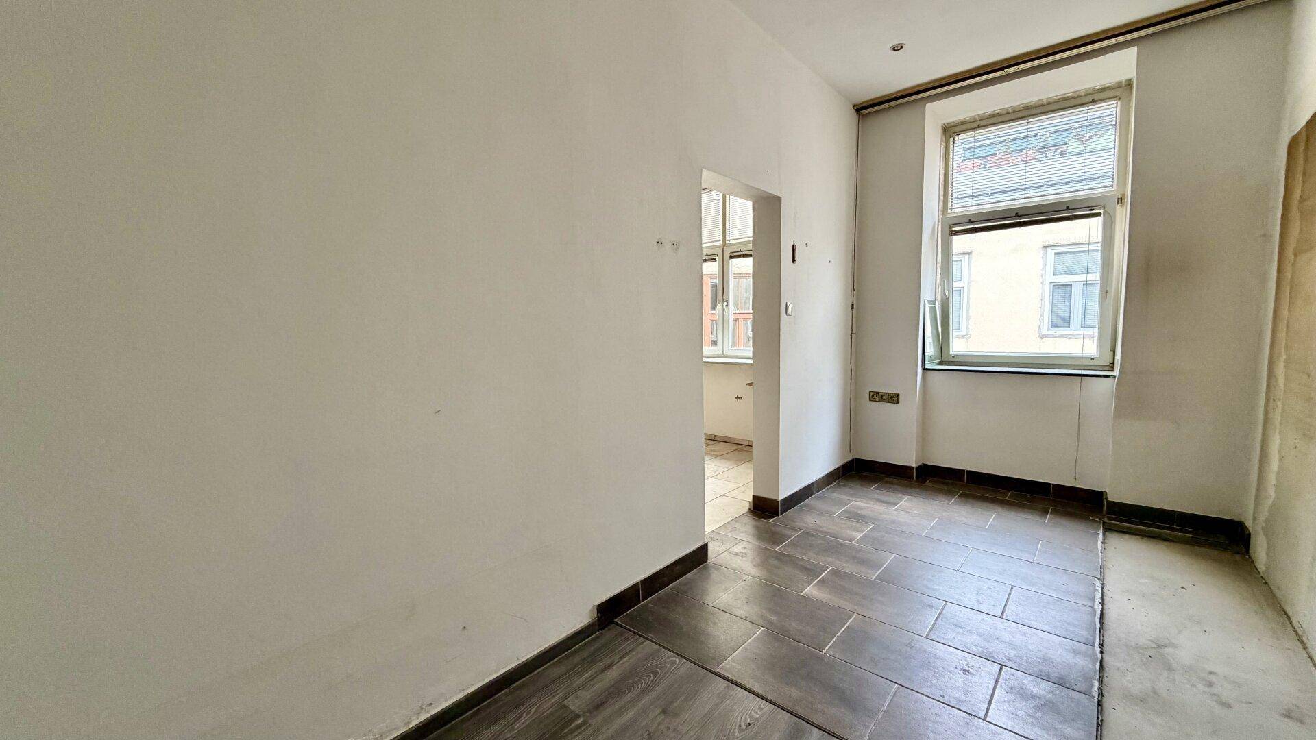 Leerer Raum mit dunklem Fliesenboden und einem Fenster, ideal für individuelle Nutzung.