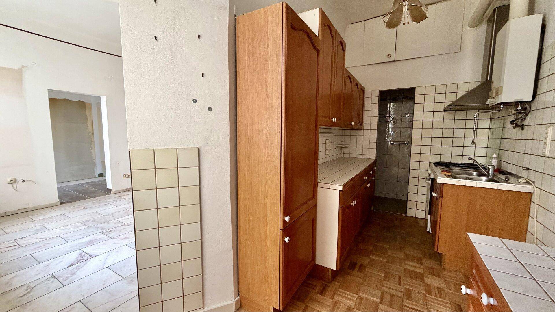 Alte Küche mit Holzschränken, gefliesten Wänden und Fischgrätparkett, renovierungsbedürftig.