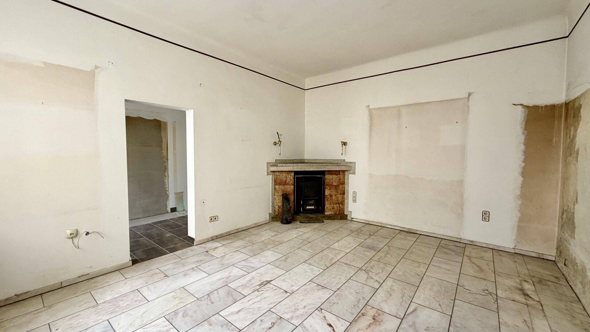 Leeres Wohnzimmer mit hellem Fliesenboden und einem gemauerten Kamin, bereit zur Renovierung.