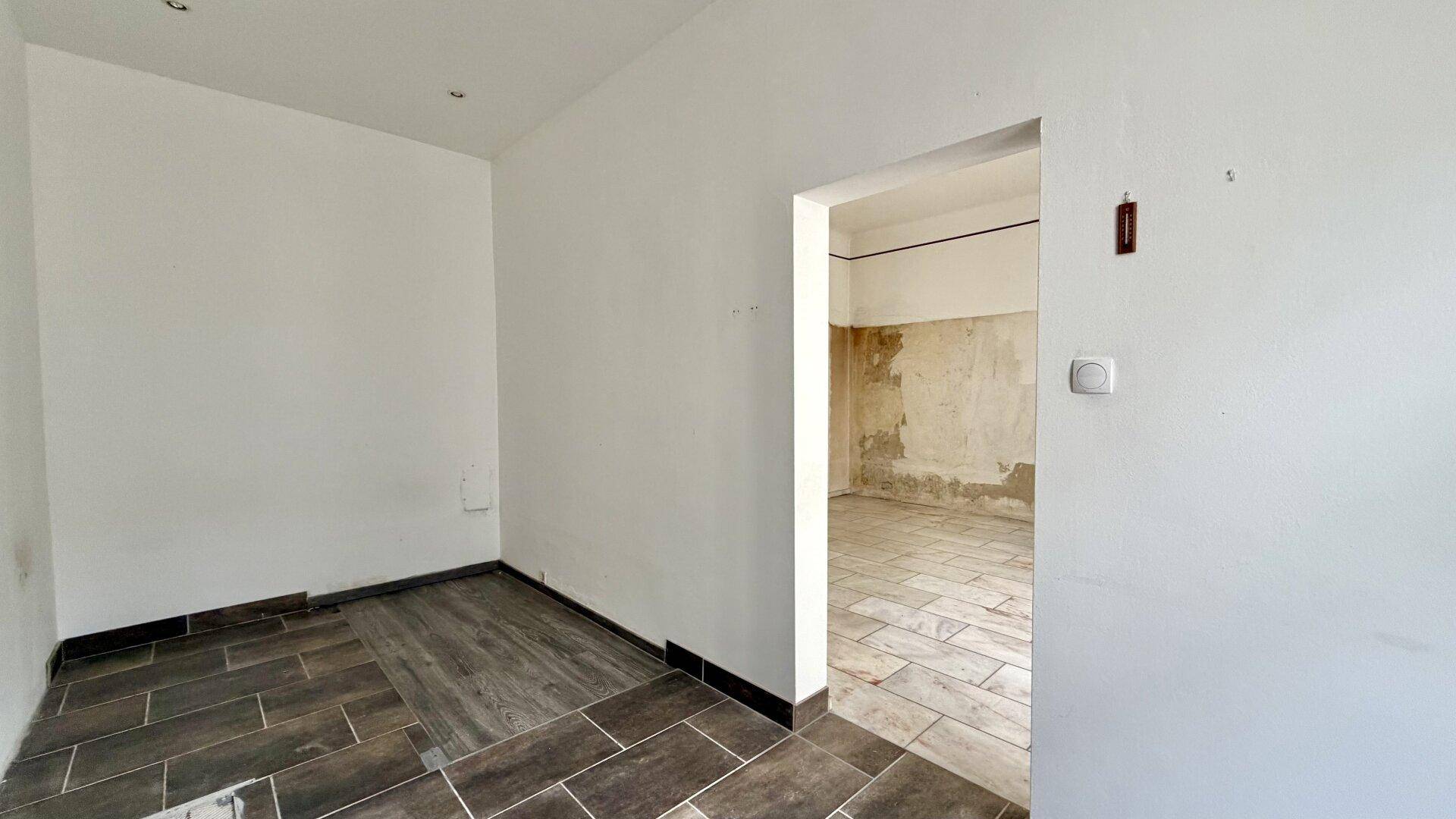 Leerer Raum mit dunklem Fliesenboden und Türöffnung zu einem weiteren Zimmer.