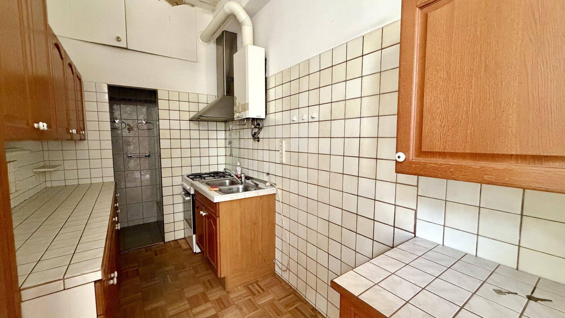 Detailansicht der alten Küche mit Spüle, Gaskochfeld, Dunstabzugshaube und Wandfliesen.