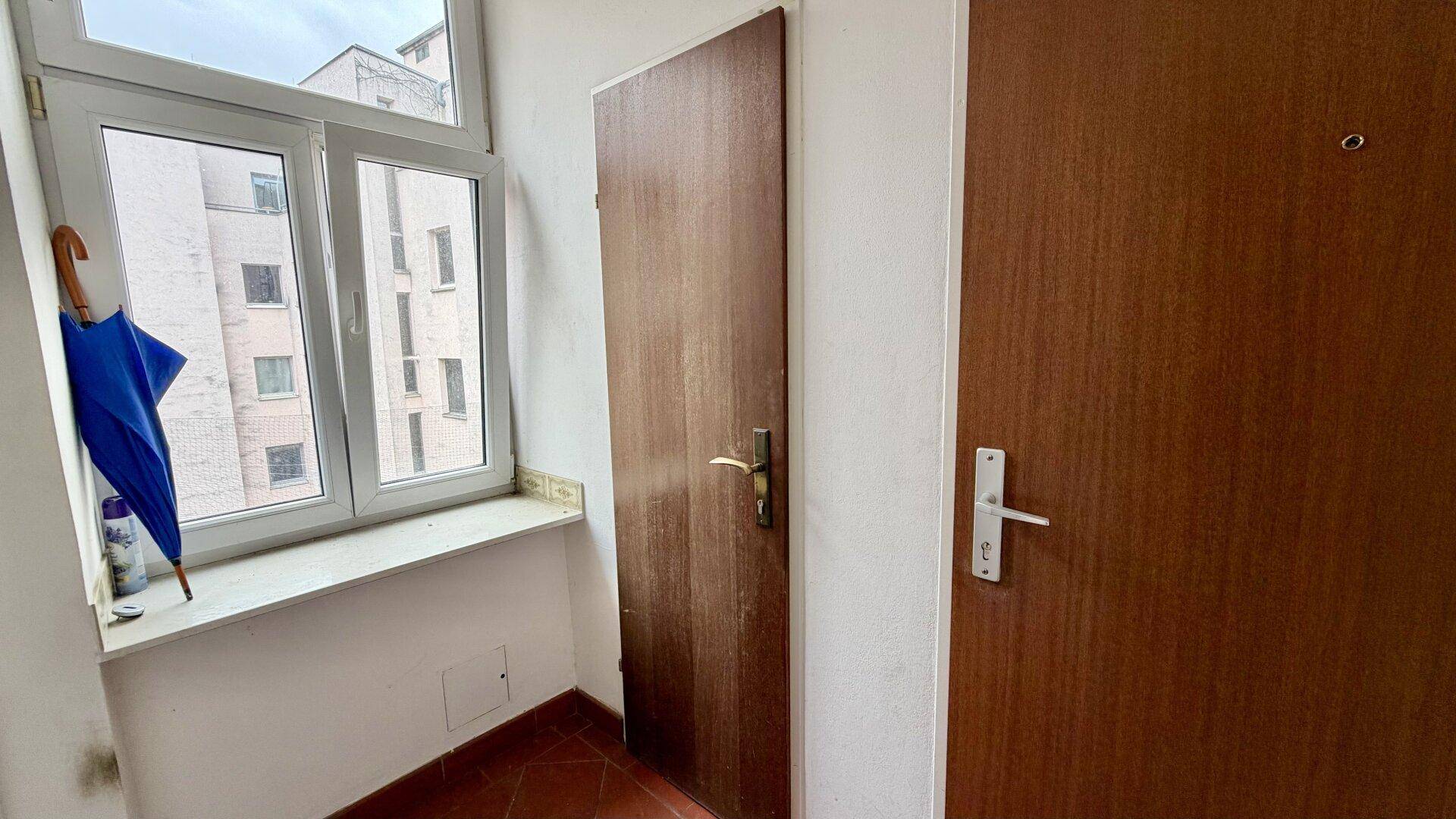 Kleiner Flur mit Fenster und zwei Holztüren, bietet natürlichen Lichteinfall.