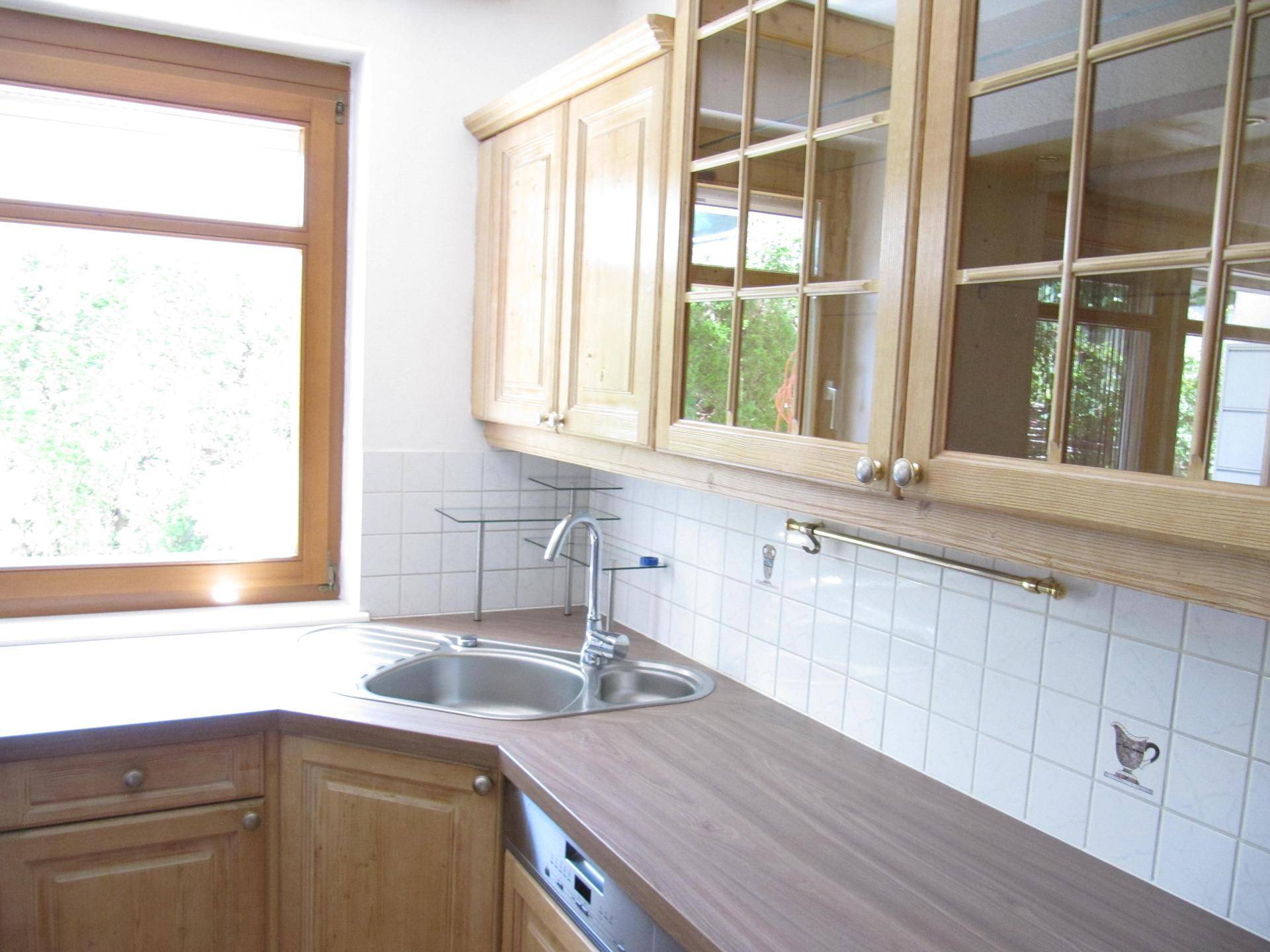 Helle Küche mit Holzschränken, Doppelspüle und Fenster, das viel Tageslicht hereinlässt.