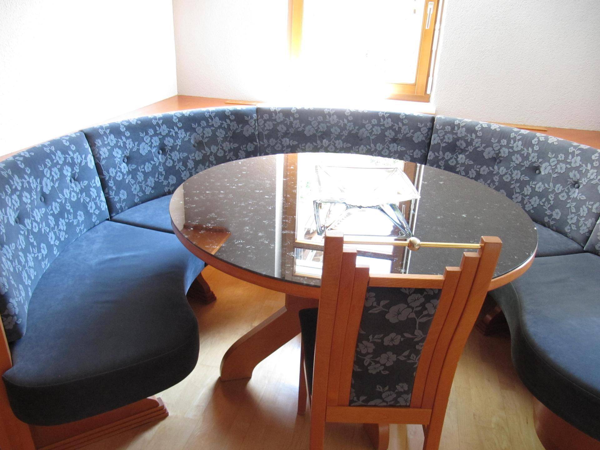 Gemütliche Essecke mit rundem Tisch und floral gemusterten Sitzbänken, ideal für Familienmahlzeiten.