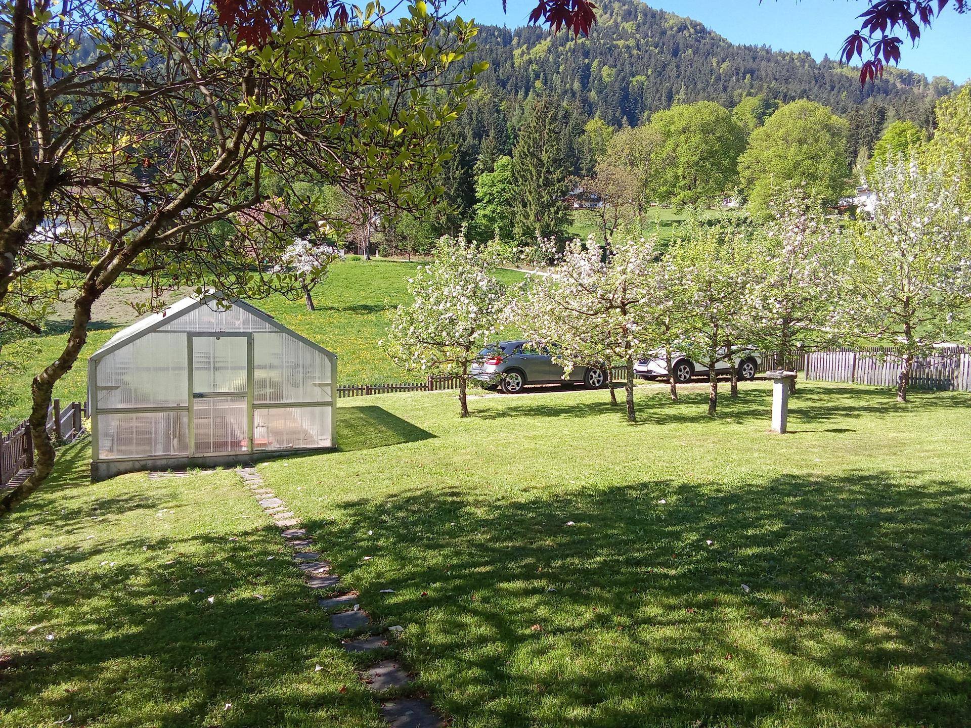 Weitläufiger Garten mit Gewächshaus, Obstbäumen und Blick auf die umliegende Berglandschaft.