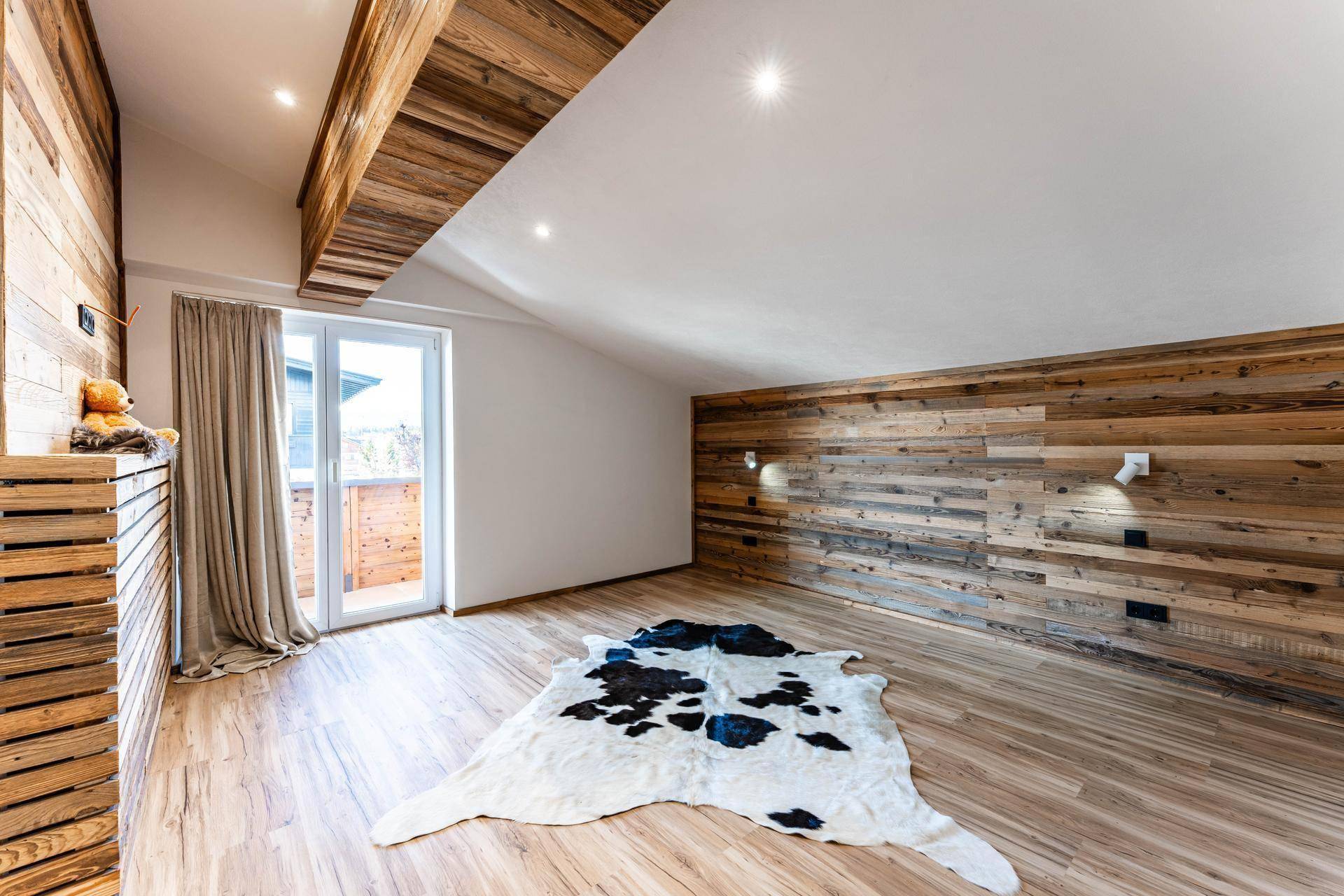 Geräumiges Schlafzimmer mit Holzwänden, Dachschräge und Zugang zum Balkon.