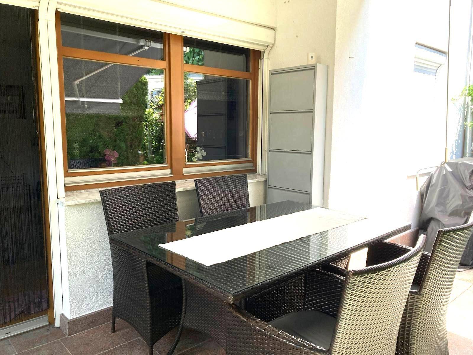Gemütlicher Essbereich auf der Terrasse mit Rattanmöbeln und Blick auf den Garten.