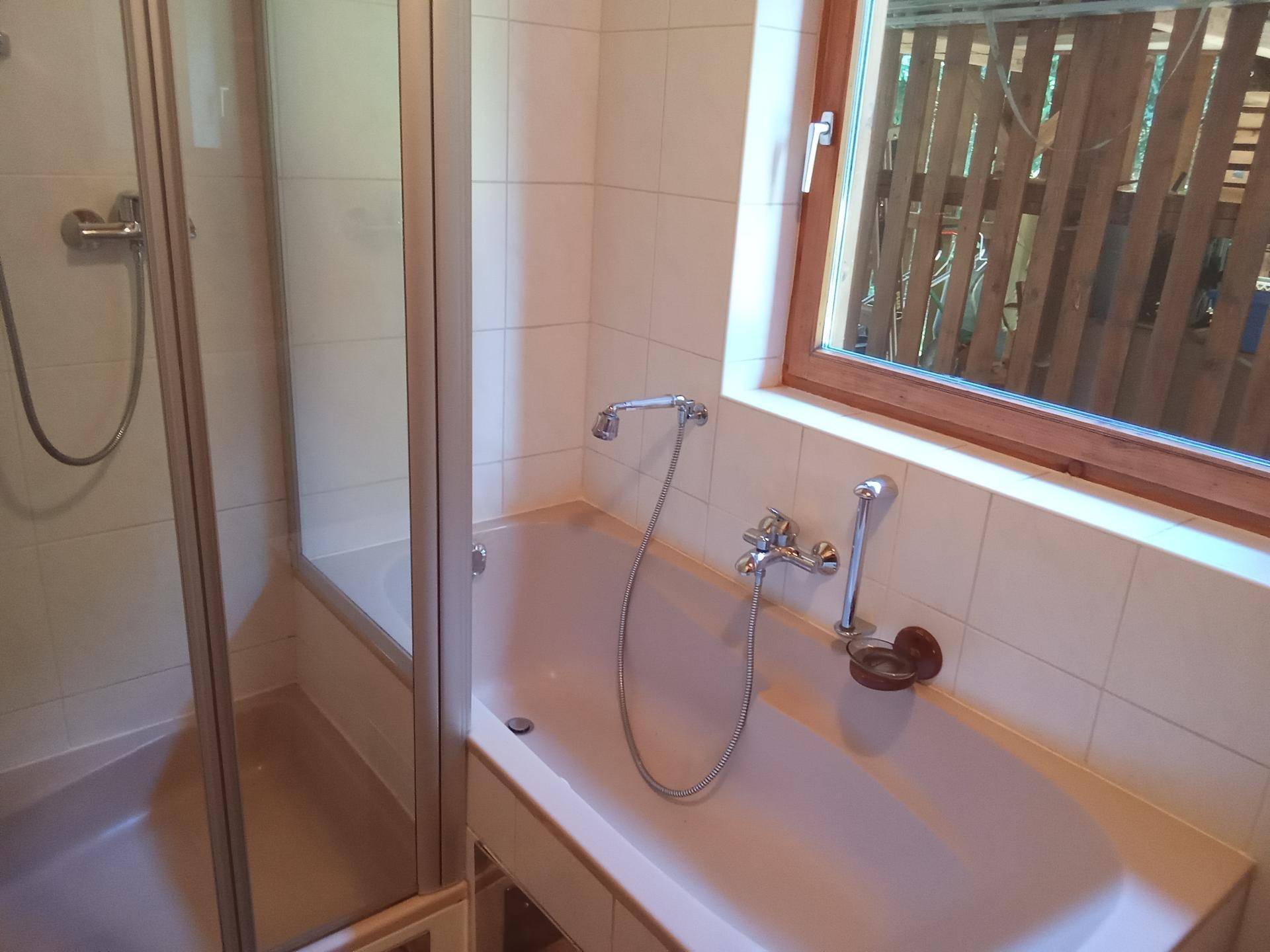 Badezimmer mit Badewanne, Duschkabine und Fenster, hell gefliest.