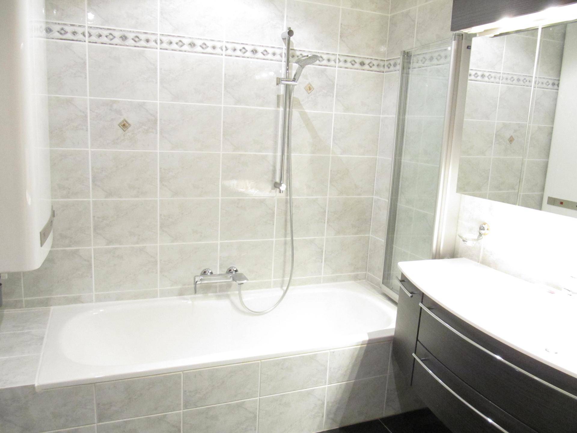 Badezimmer mit Badewanne, Duschvorrichtung und hellen Fliesen, praktisch und funktional gestaltet.