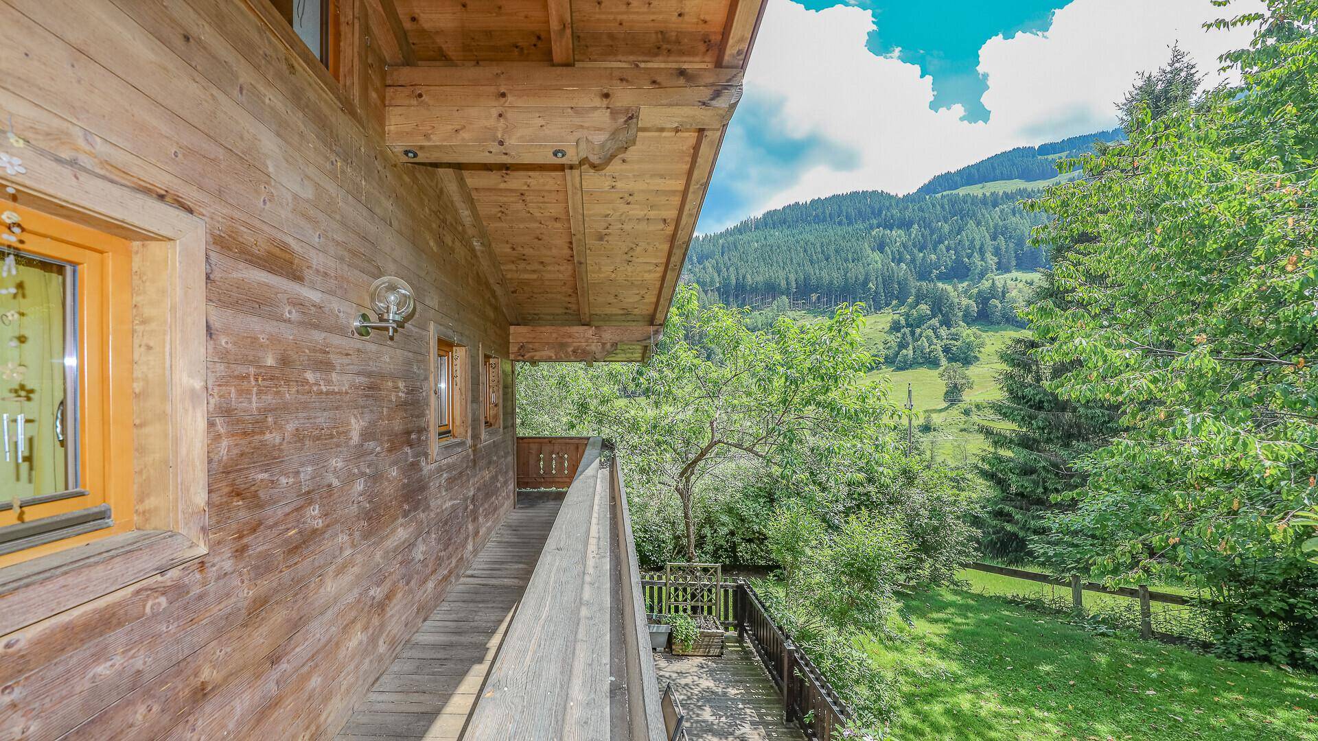 Langer Holzbalkon mit Blick auf die grüne Berglandschaft und umliegende Natur.