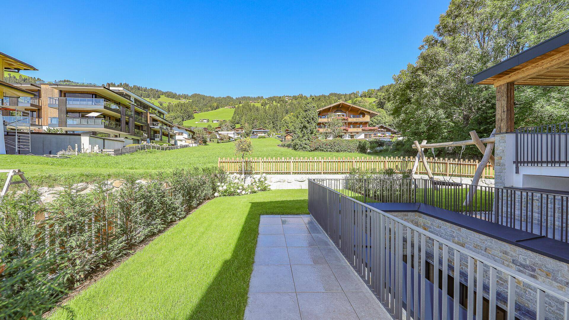 Gepflegter Gartenbereich mit Rasenfläche, Hecken und Kinderschaukel im Grünen.